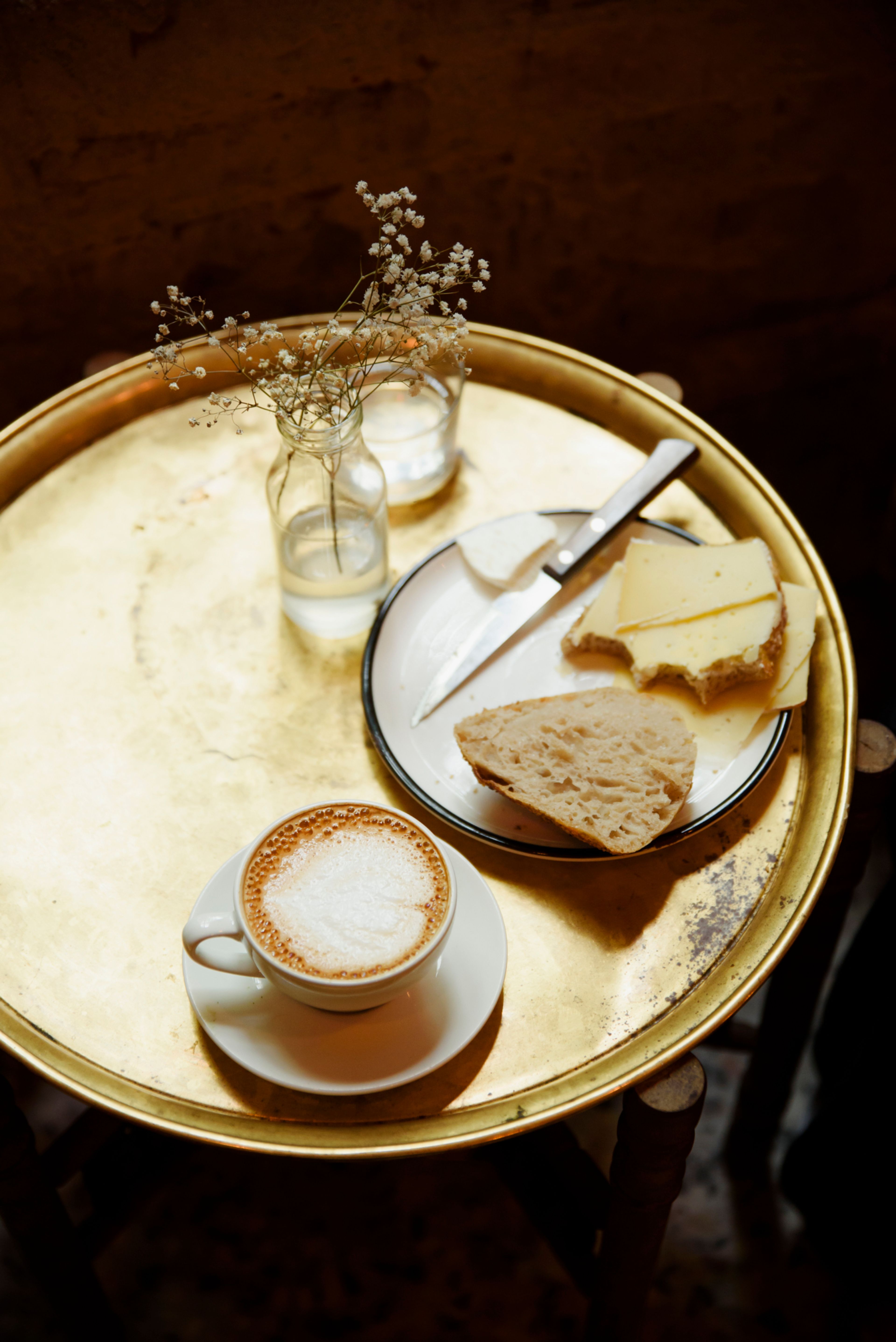 Bilde av et kafébord med en kaffekopp, tallerken med brødmat og en blomst på