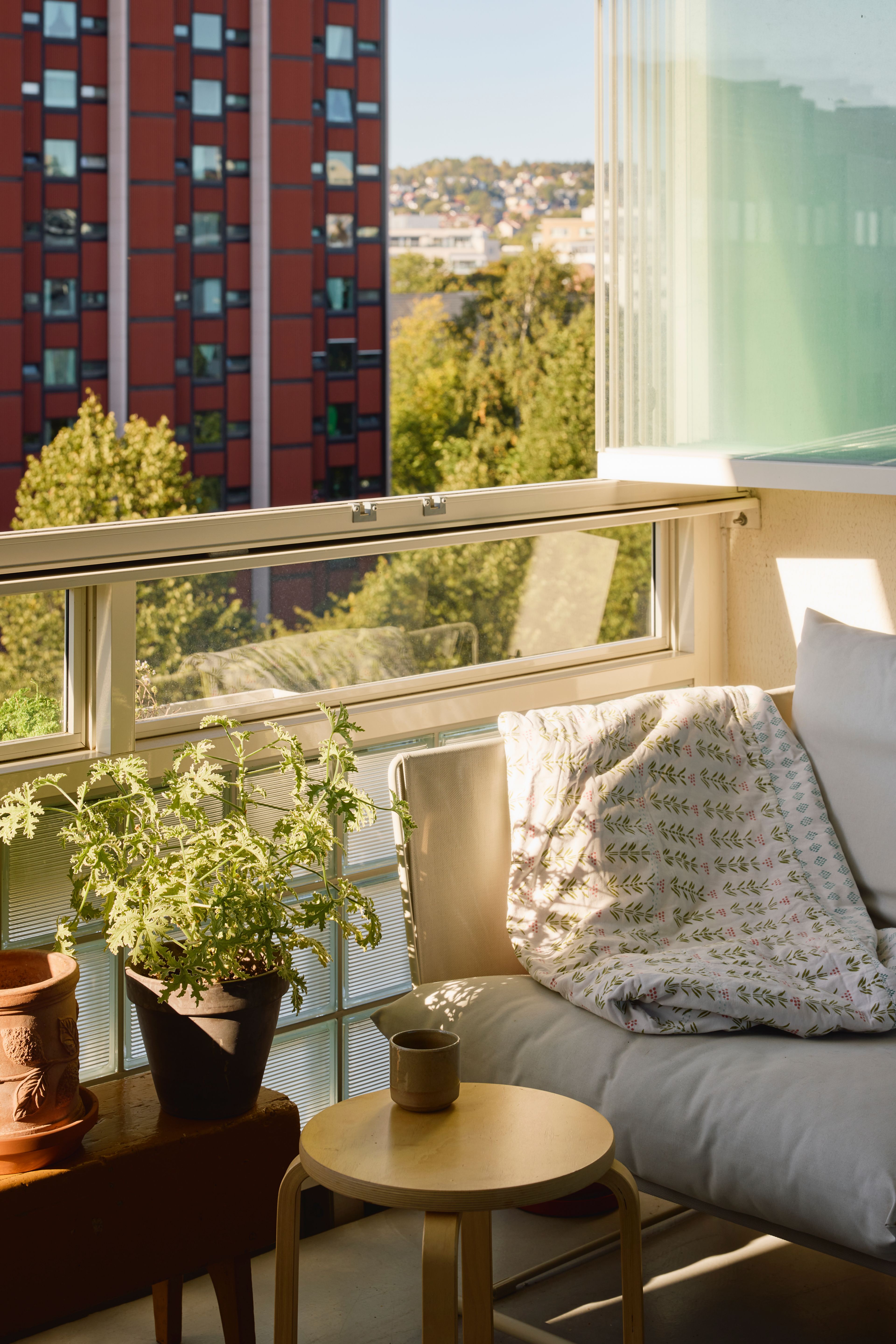 Nærbilde fra balkong med en utesofa, et rundt bord og en grønn plante. 