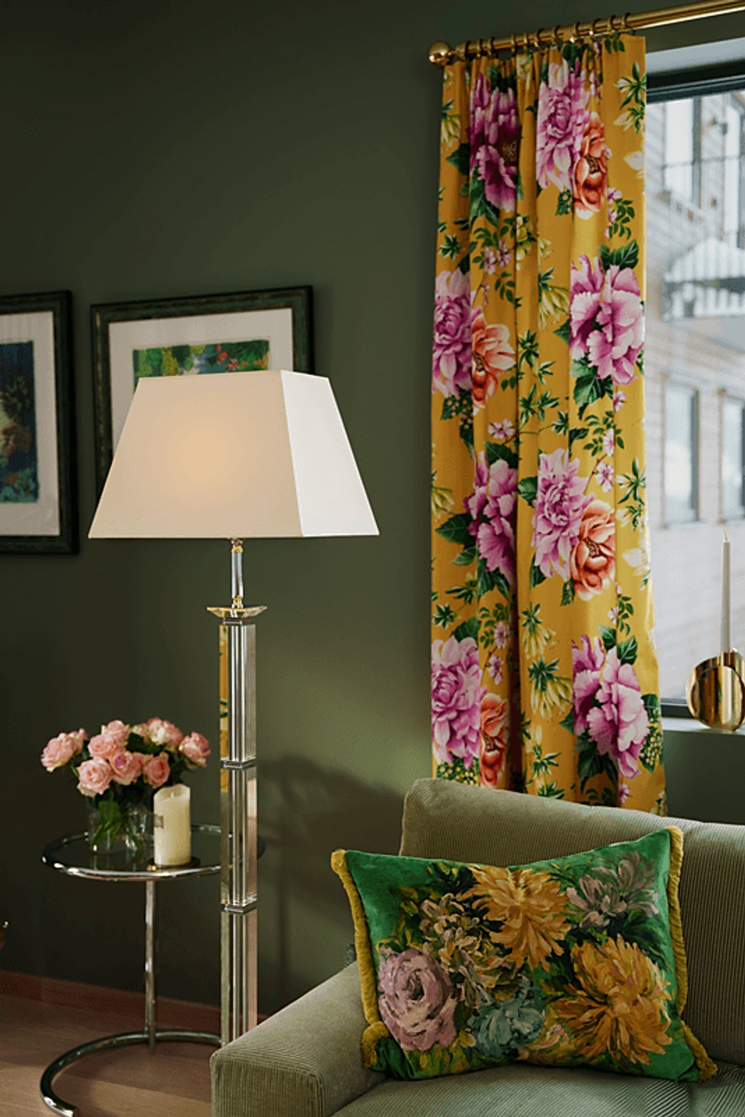Detaljbilde av den ene stuelampa mot den grønne veggen og sofaen, til høyre for noen gulblomstrede gardiner