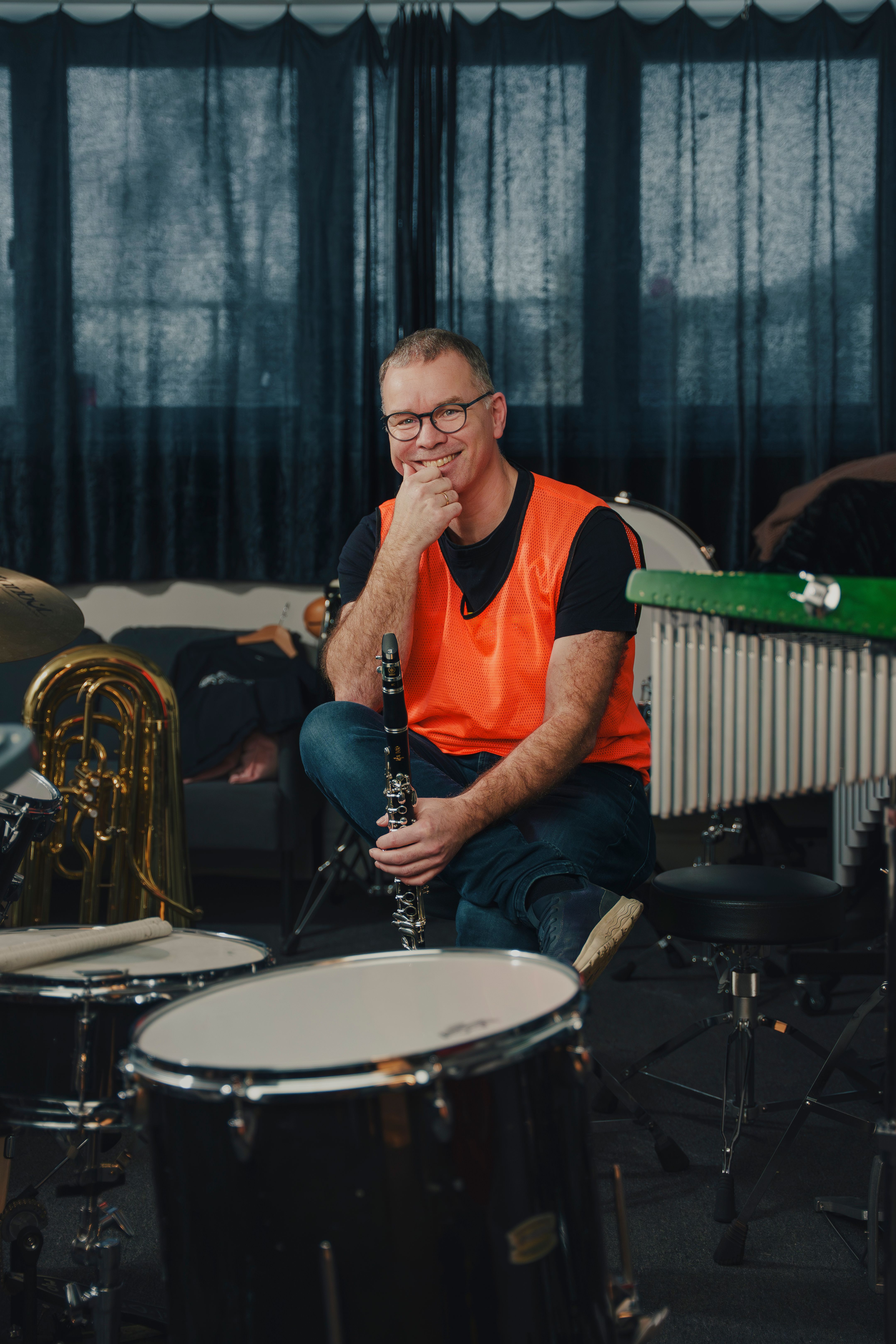Per Christian Kittilsen sitter omgitt av trommer, klarinett, marimba og tuba i et korpsrom, med klarinett i hånda.