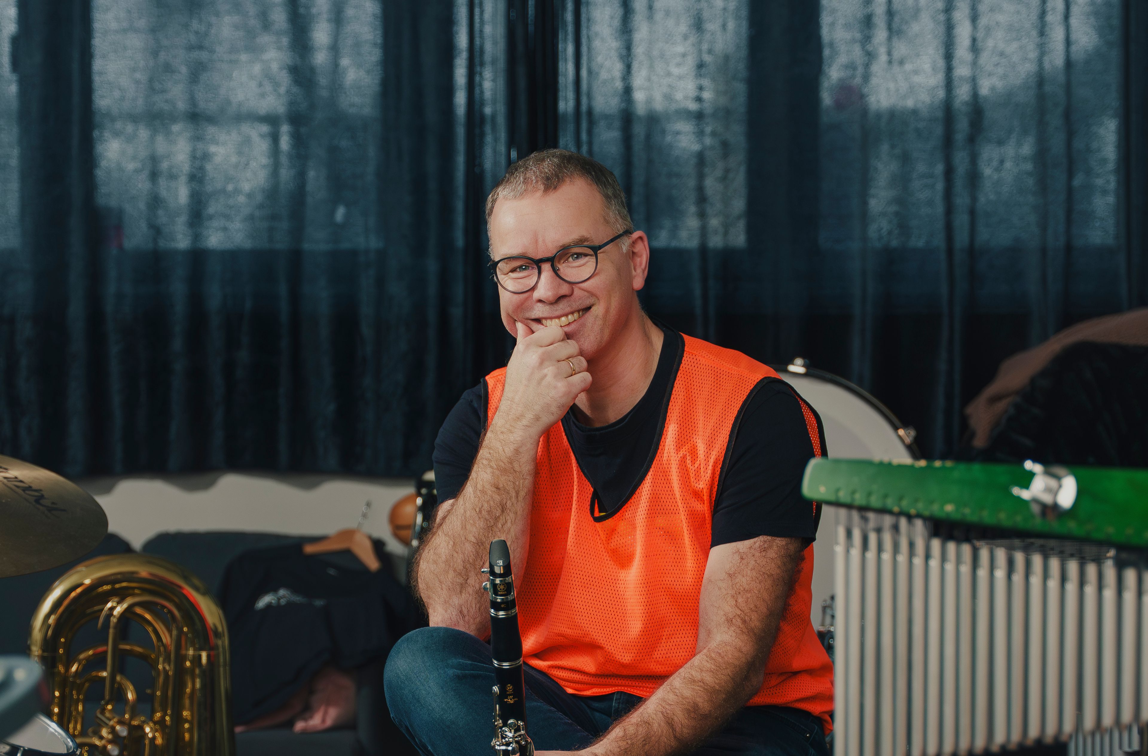 Per Christian Kittilsen sitter omgitt av trommer, klarinett, marimba og tuba i et korpsrom, med klarinett i hånda.
