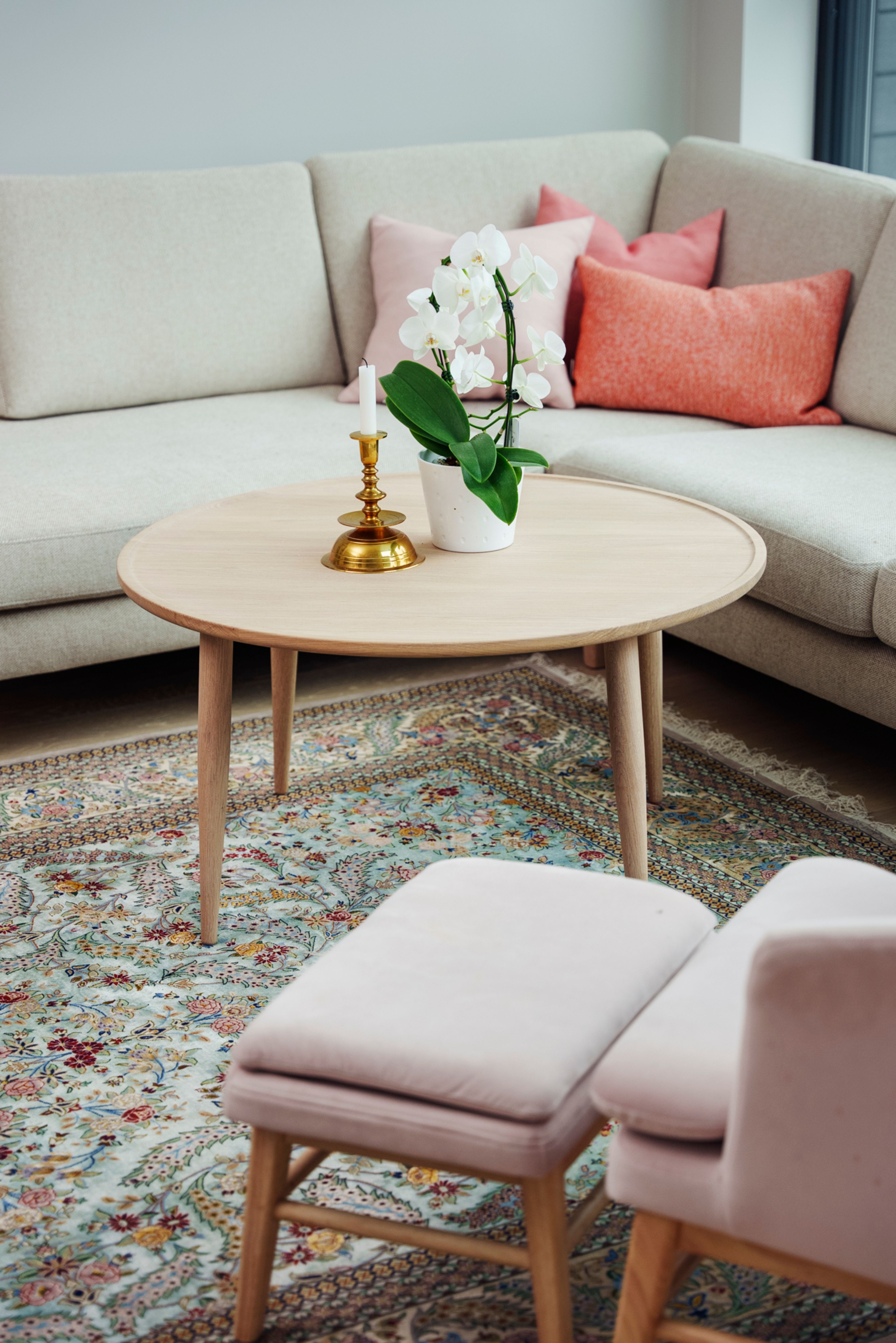 Et bilde av interiøret i hjemmet til Nina på Vitigrend. Hun har et mønstret teppe, et lyst bord i eik og en lyserosa stol. I bakgrunnen står en grå sofa med rosa puter.