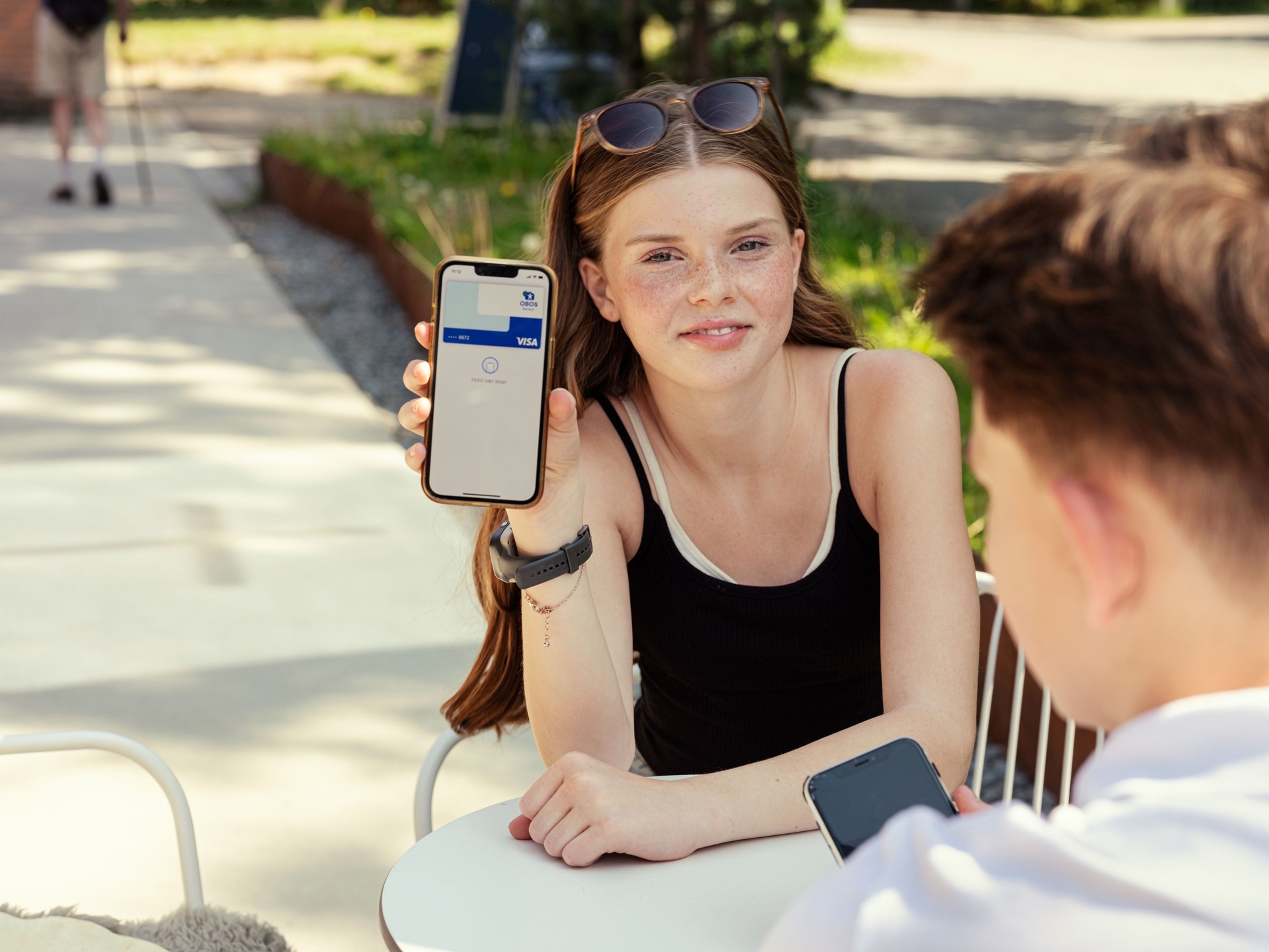 En ung jente holder opp mobiltelefonen sin med OBOS-bankkort som apple pay
