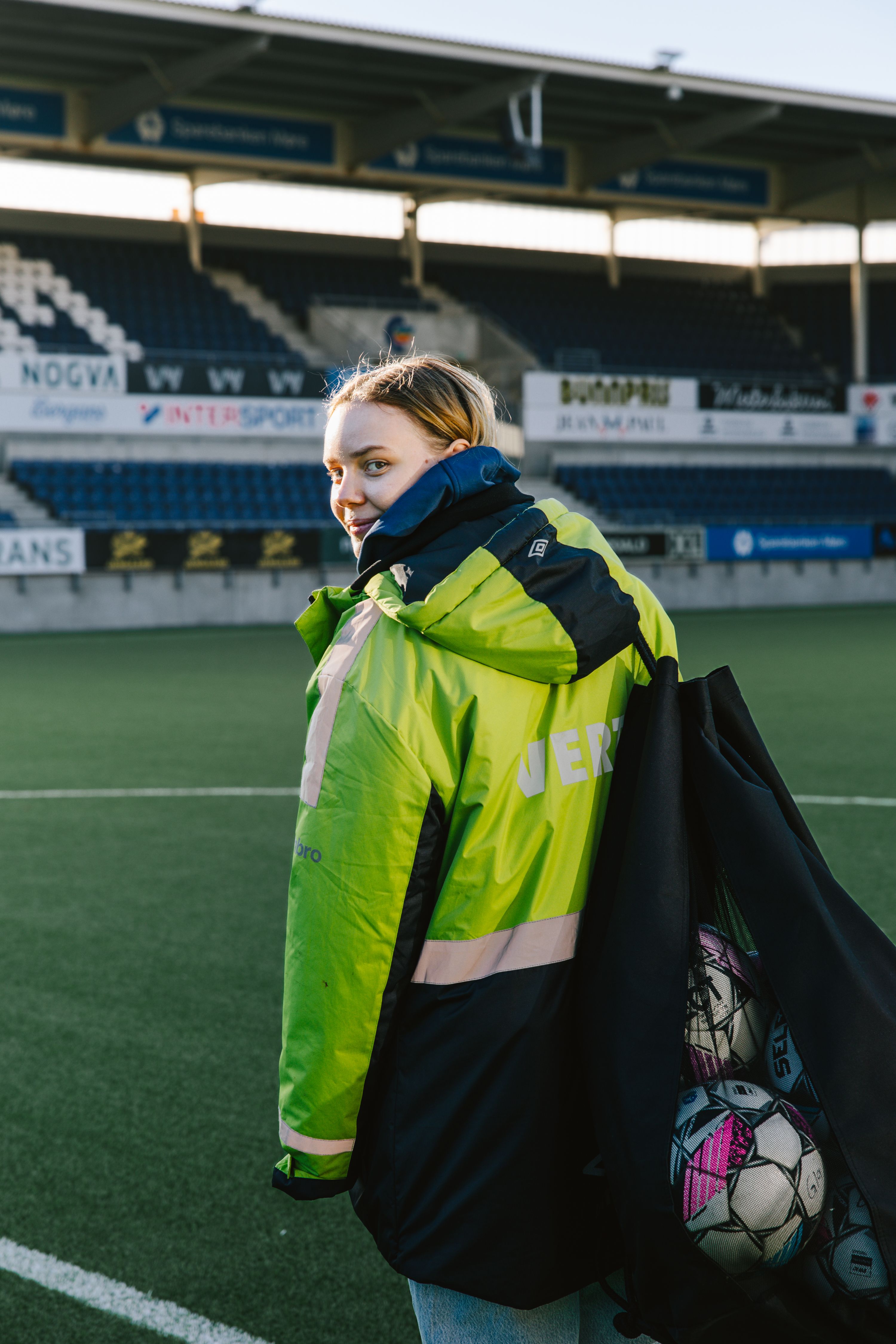 Kristina Aarseth Sætre på Color Line Stadion med neongul målvakt-jakke og en nettbag med fotballer over skulderen, klar for kamp.