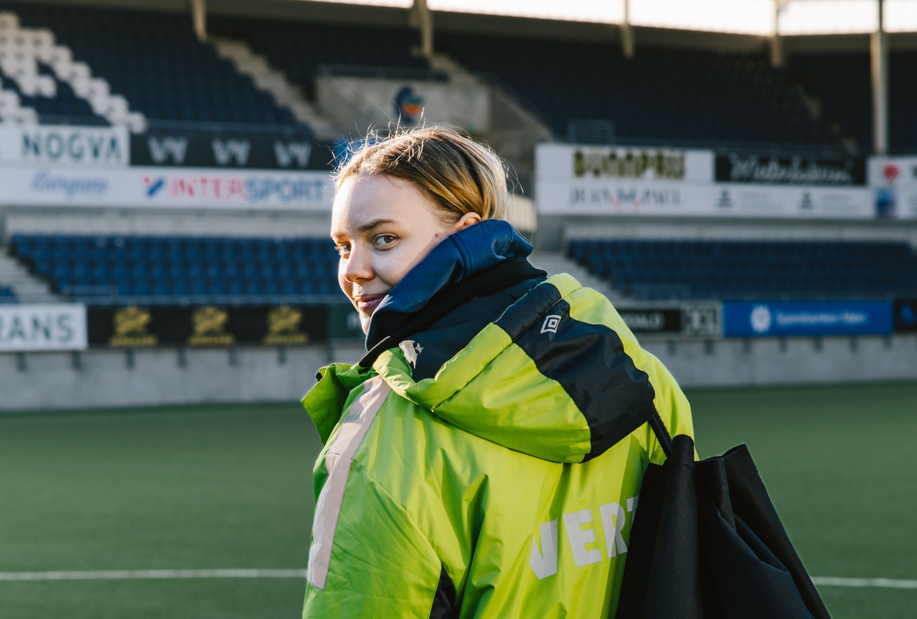 Kristina Aarseth Sætre på Color Line Stadion med neongul målvakt-jakke og en nettbag med fotballer over skulderen, klar for kamp.