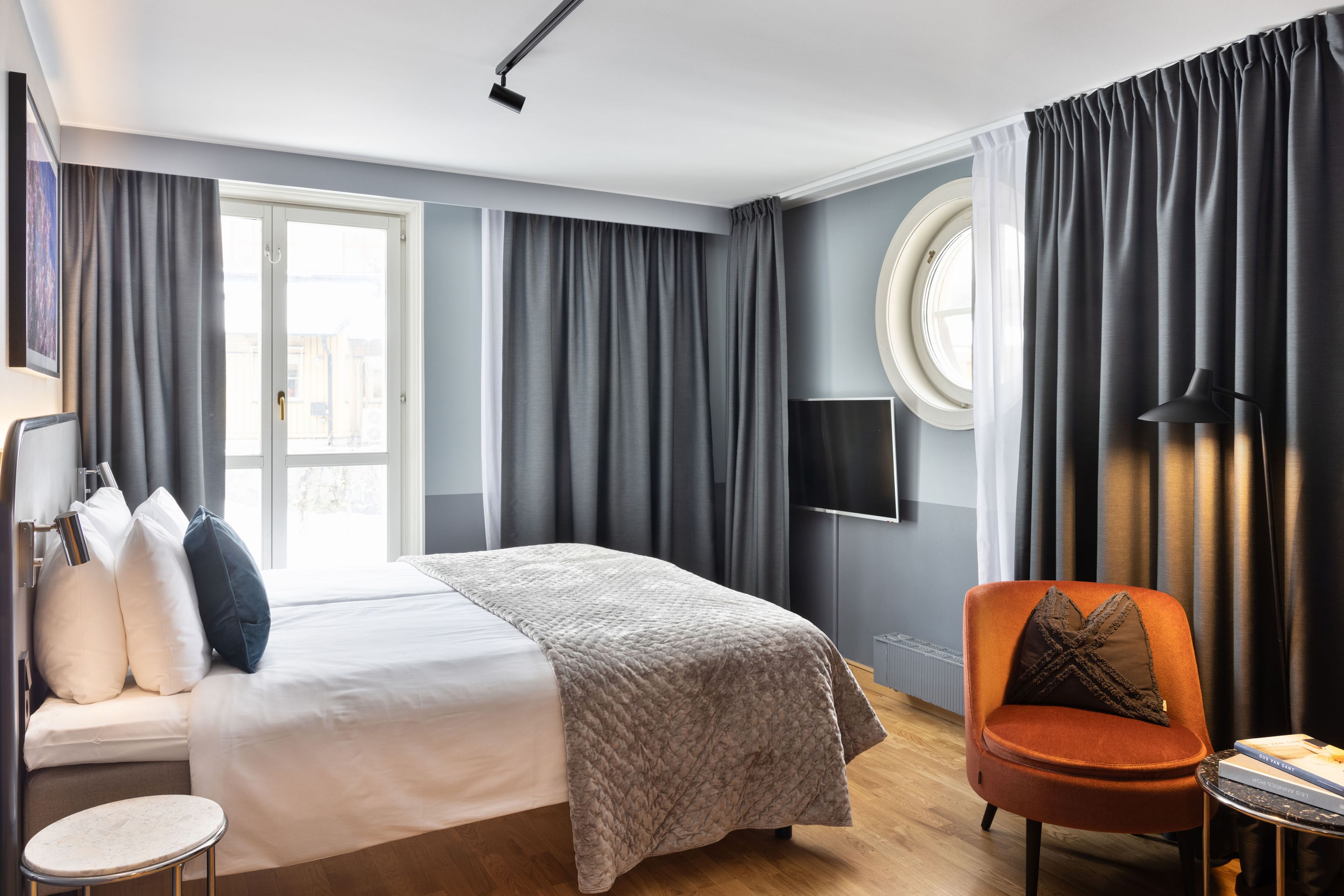 Hotelrom hos Hasselbacken hotell. Innbydende blått rom med en dobbelseng og grå gardiner.