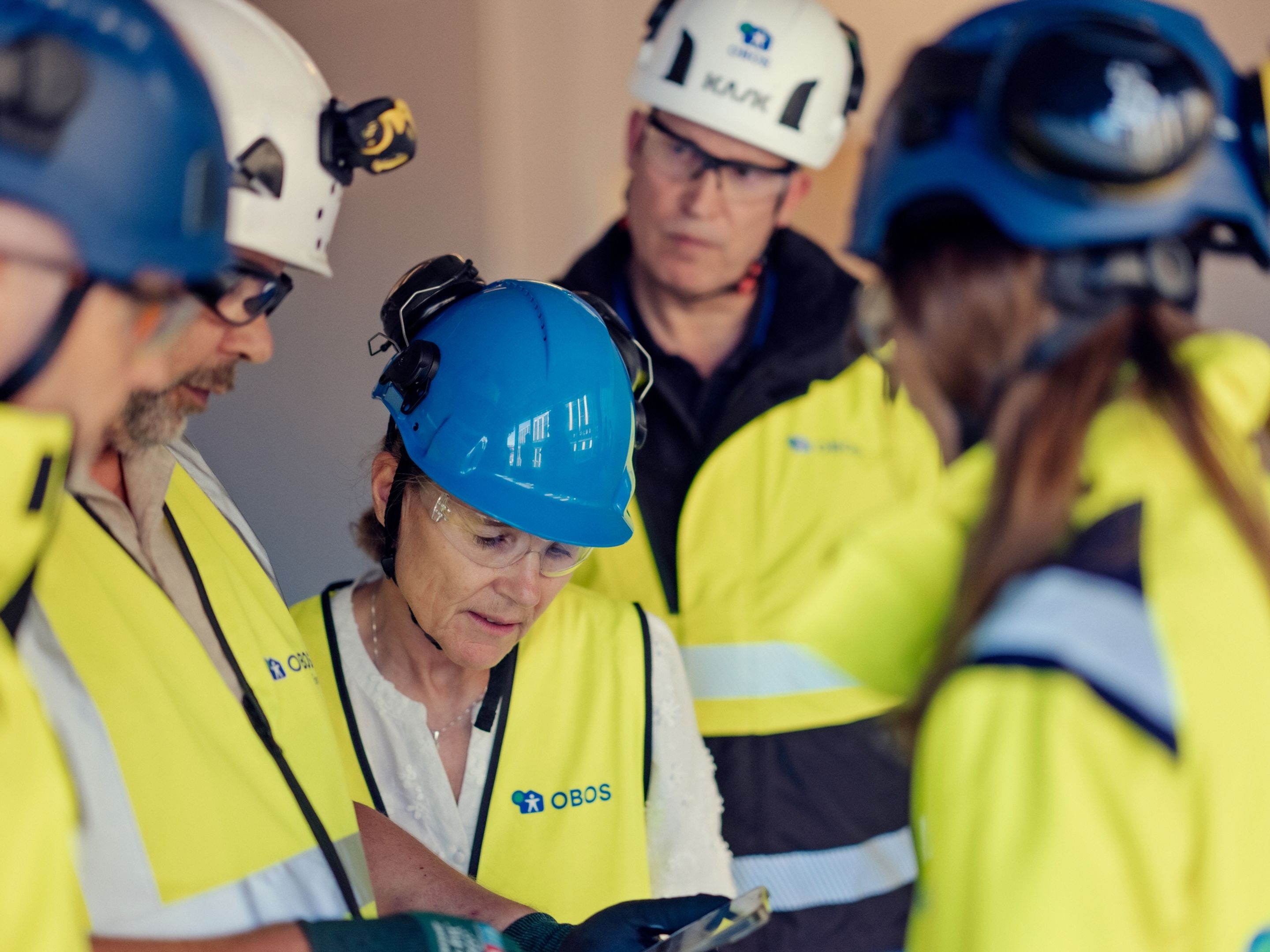 a group of construction workers wearing hard hats and safety vests are standing in a circle .