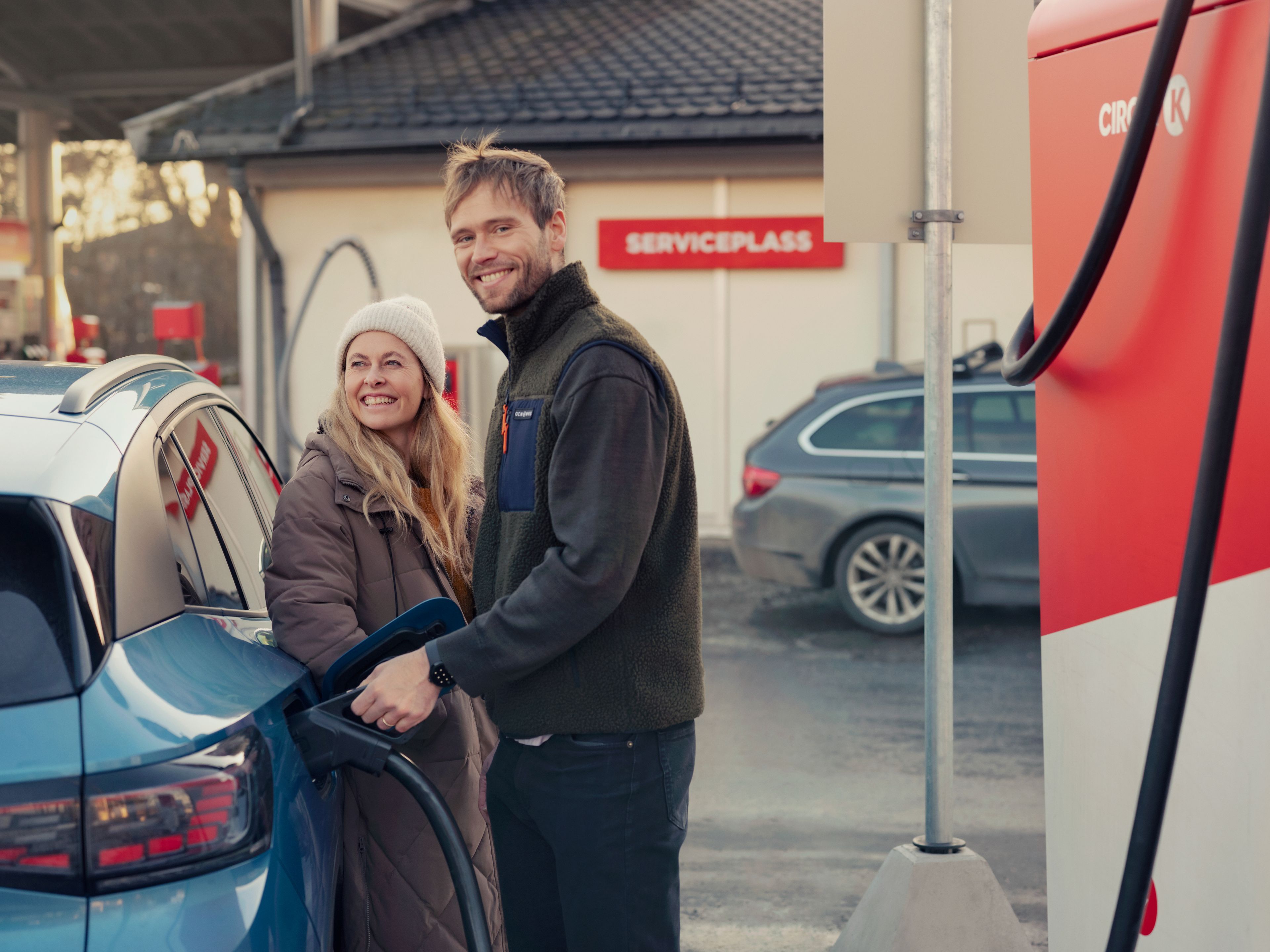 En mann og en dame lader bilen på Circle K. De smiler.