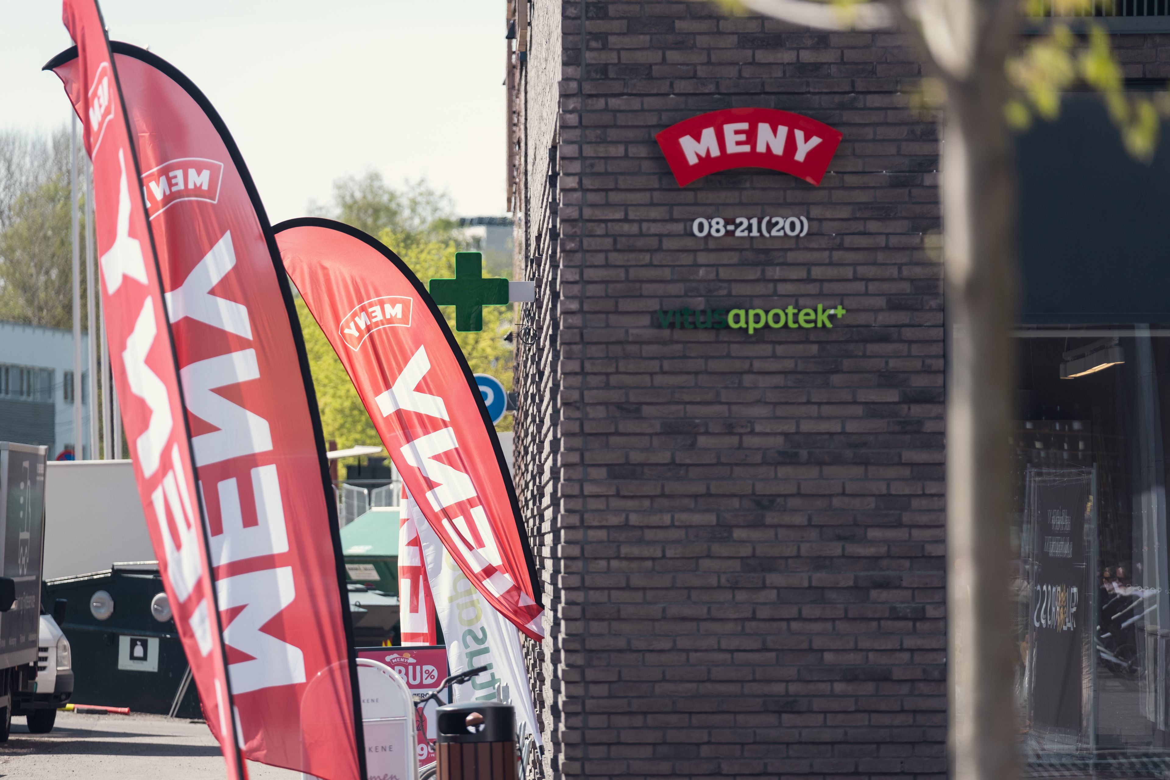 Inngang til nærsenteret på Frysja med blant annet Meny og Vitus apotek. Det er store Meny-flagg ved inngangen.