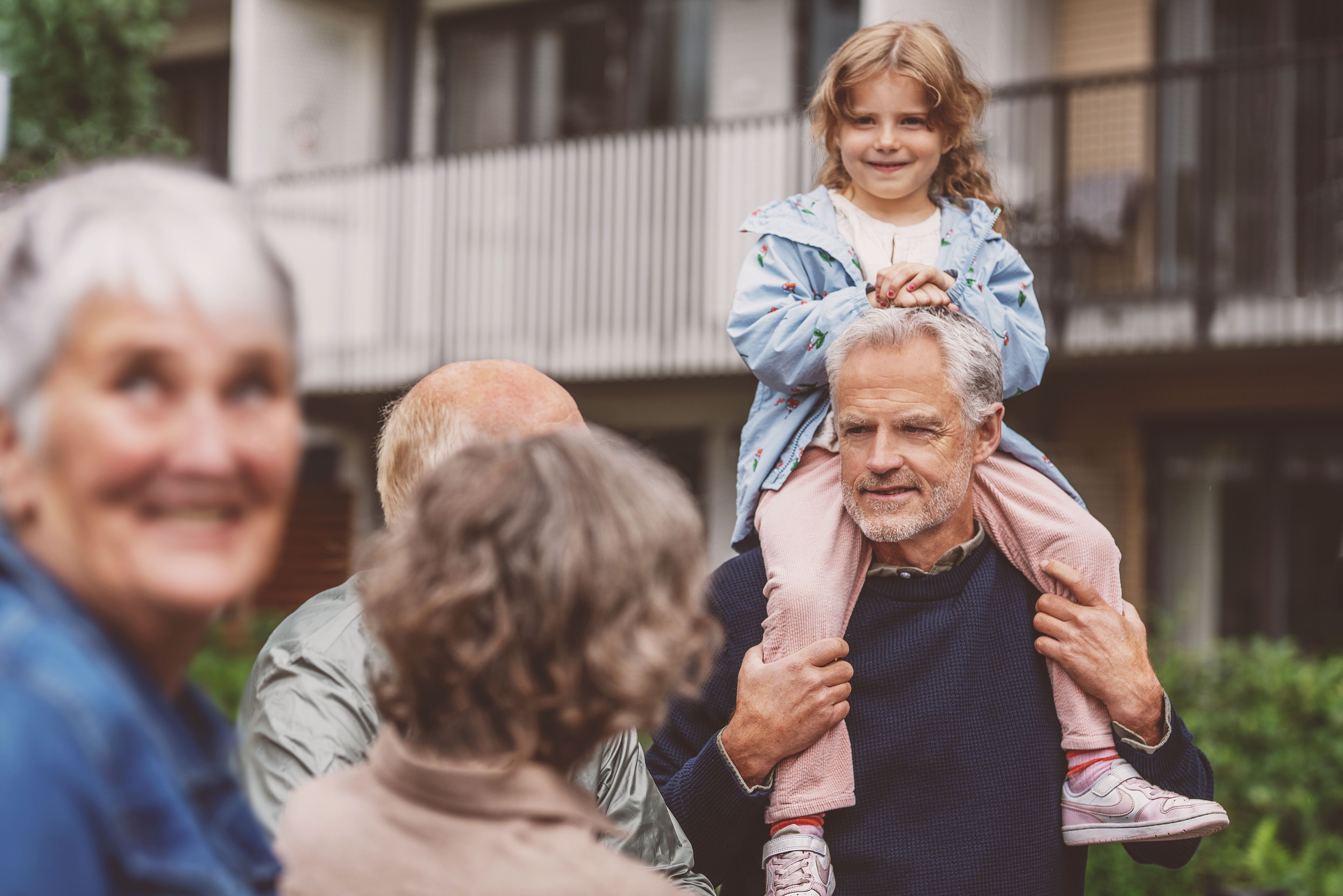 En mann har barnebarnet på skuldrene. Det står flere folk rundt han.