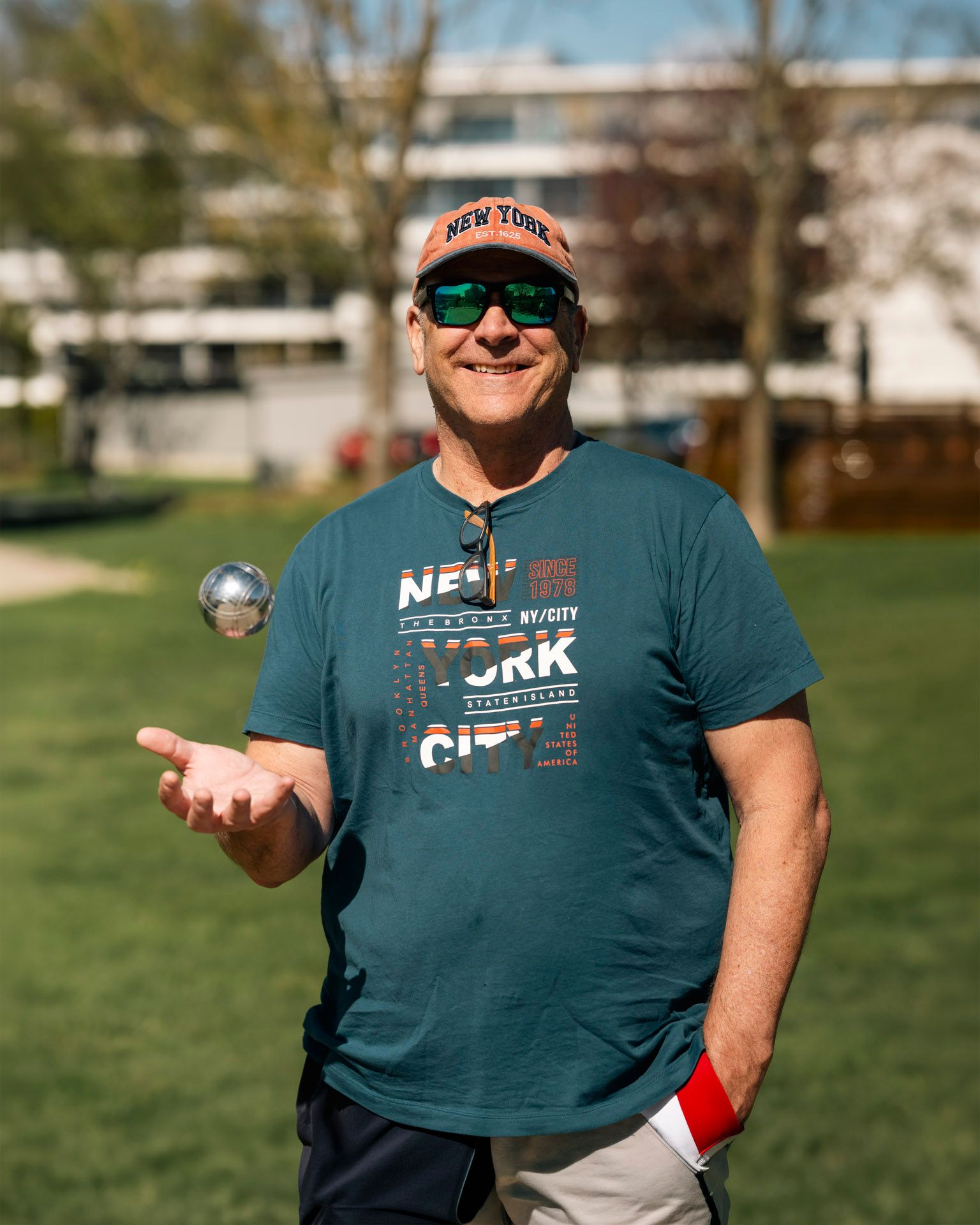 Mann står på gressplen i et boligområde og holder en petanquekule i hånden.