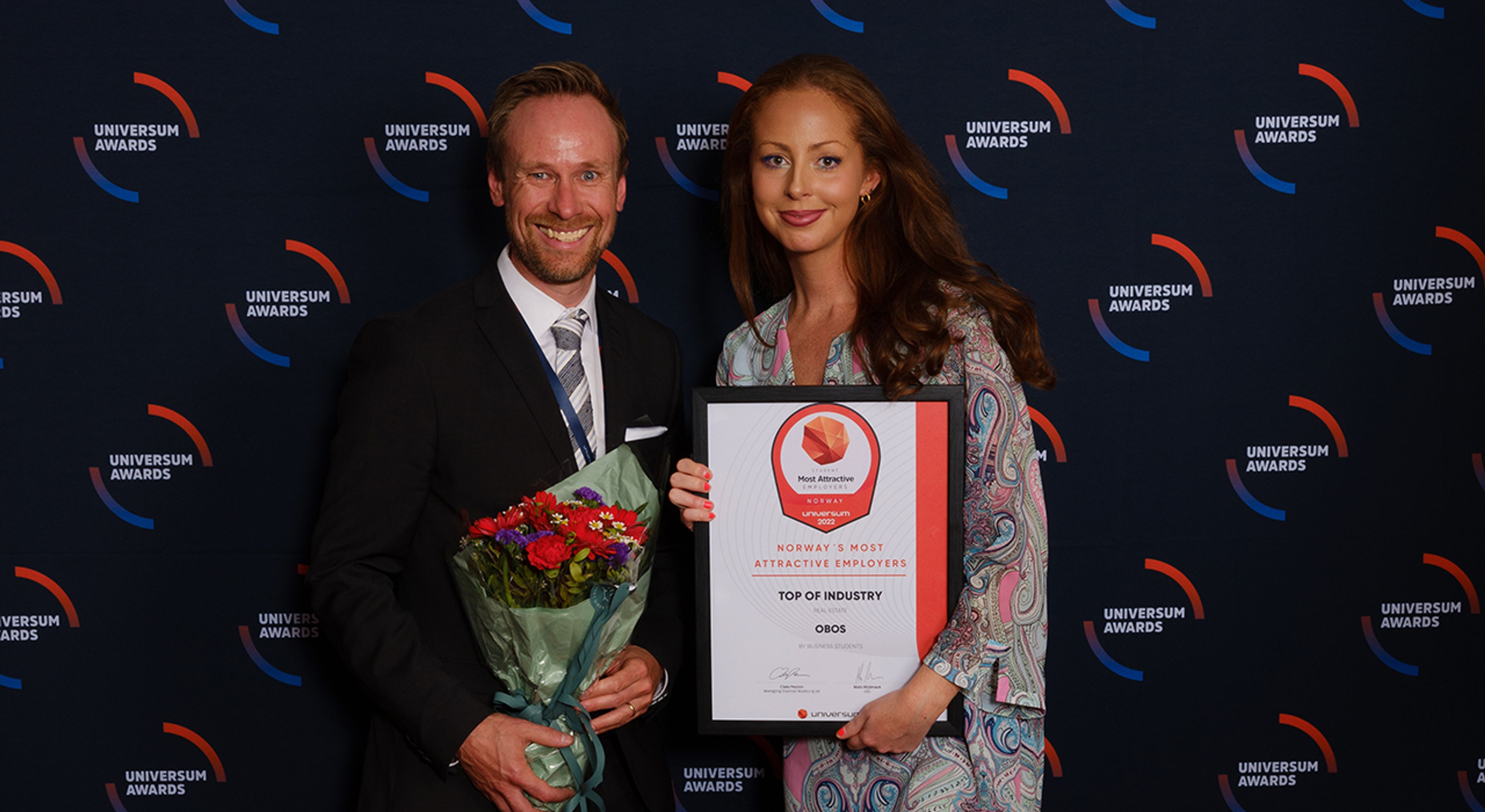 To personer som holder et diplom og en blomsterbukett