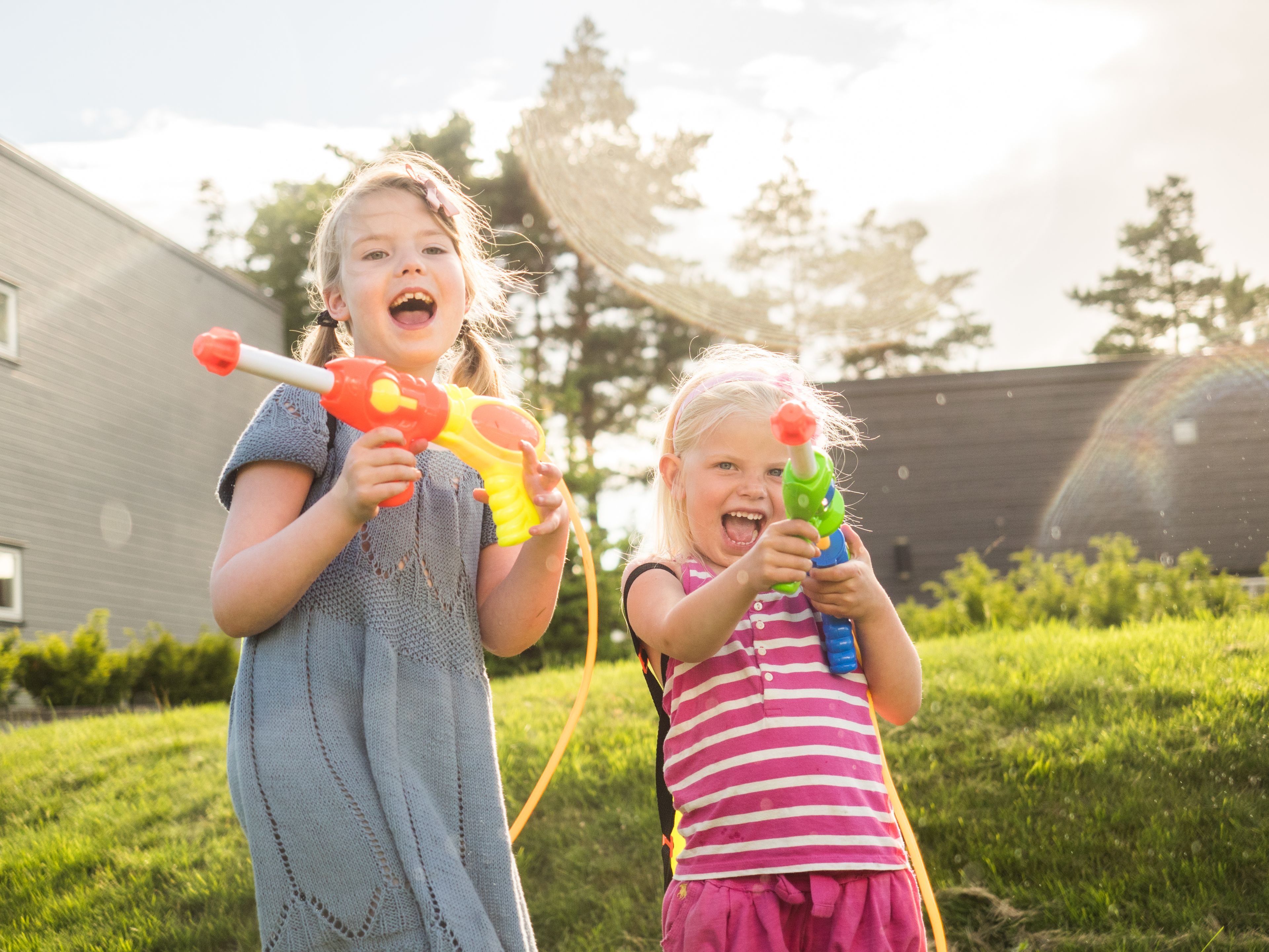 To små jenter leker med vannpistoler i hagen.