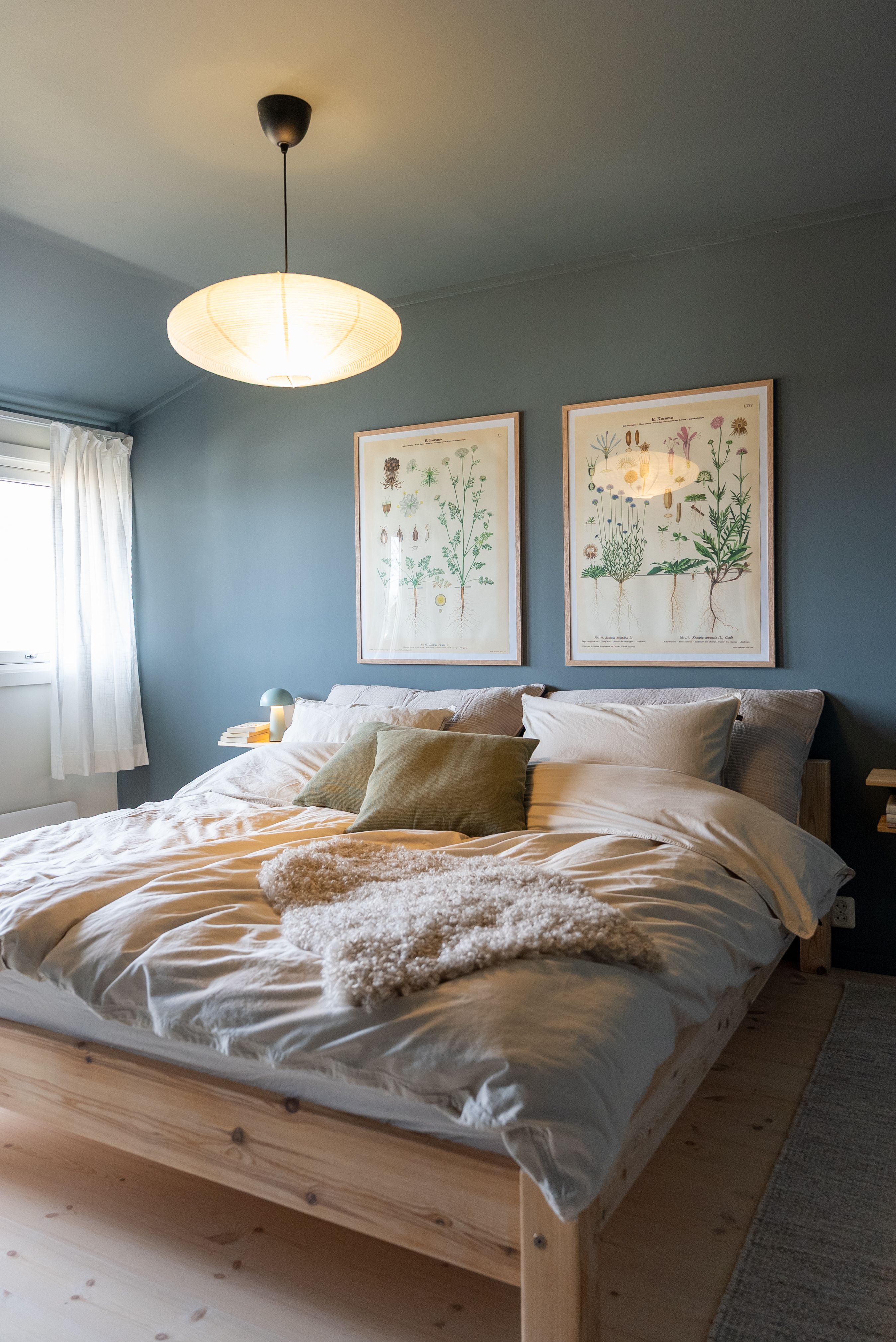 Et nyoppusset soverom med nymalte vegger, heltre furugulv og pent oppredd seng.