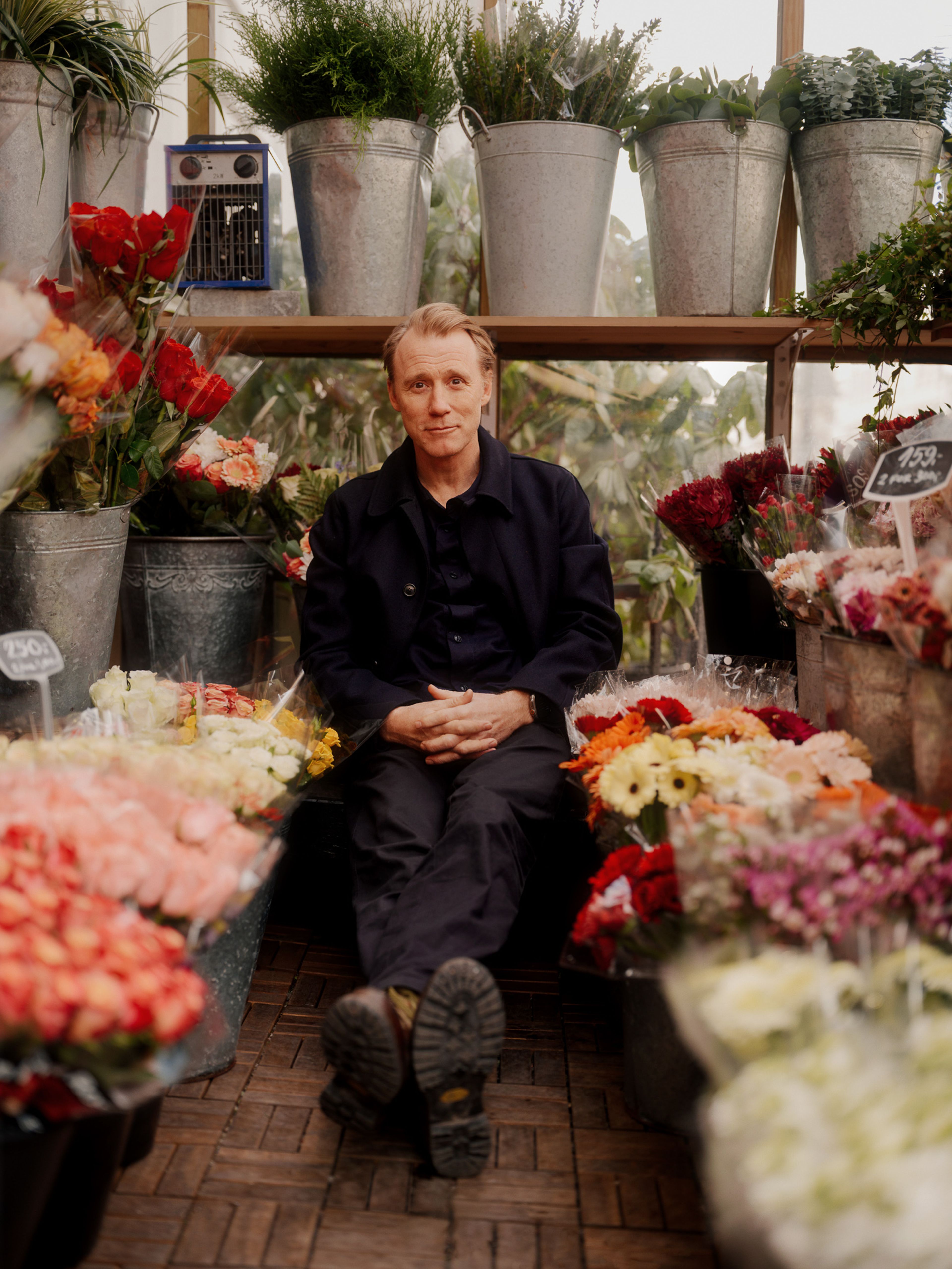 Thorbjørn Harr sitter på bakken mellom blomsterbuketter i en blomsterbutikk.