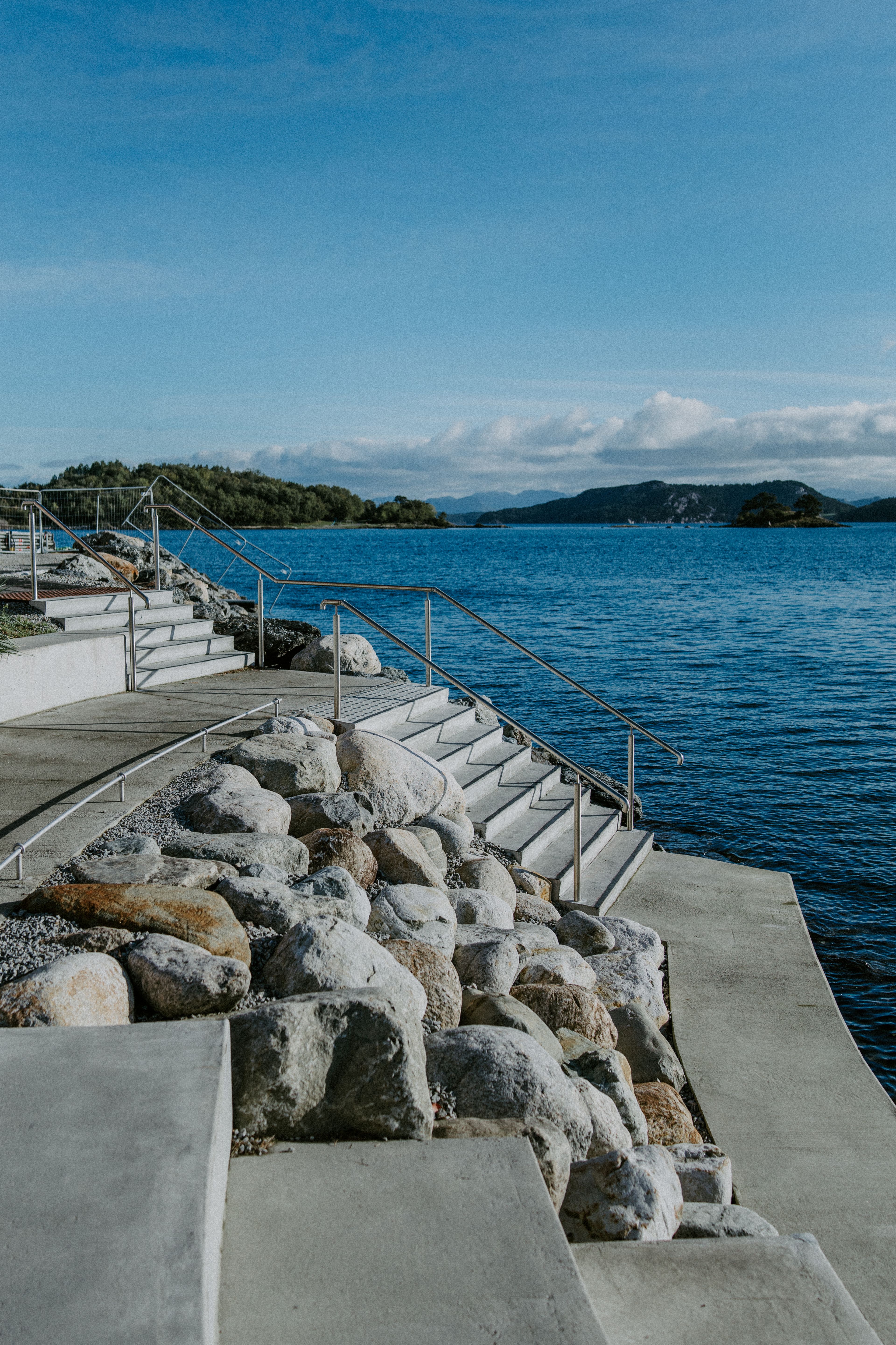 Brede betongtrapper ned i sjøen langs strandkanten på Odden, med holmer og blå himmel bak.