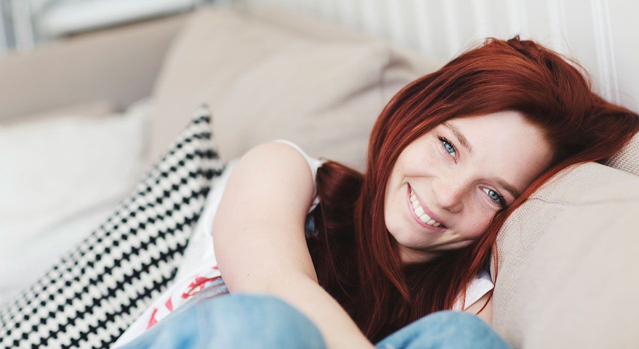 En smilende ung kvinne sitter i en beige sofa