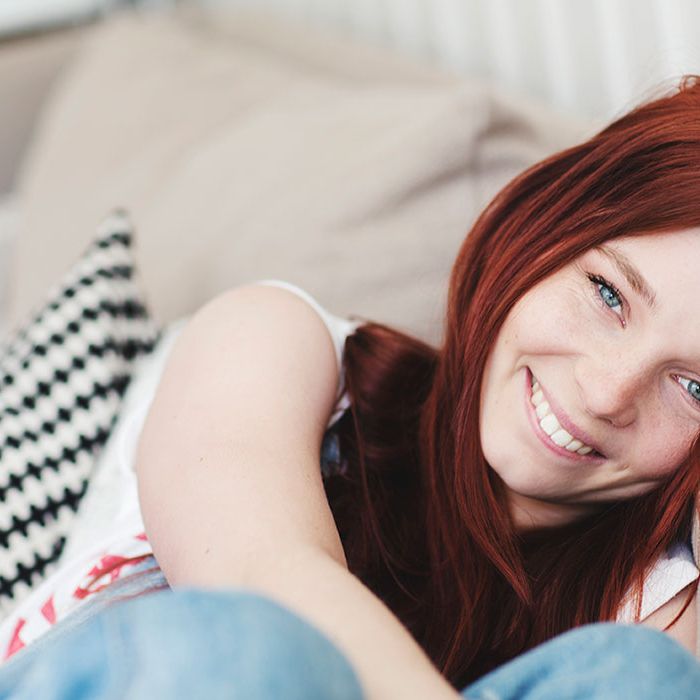 En smilende ung kvinne sitter i en beige sofa