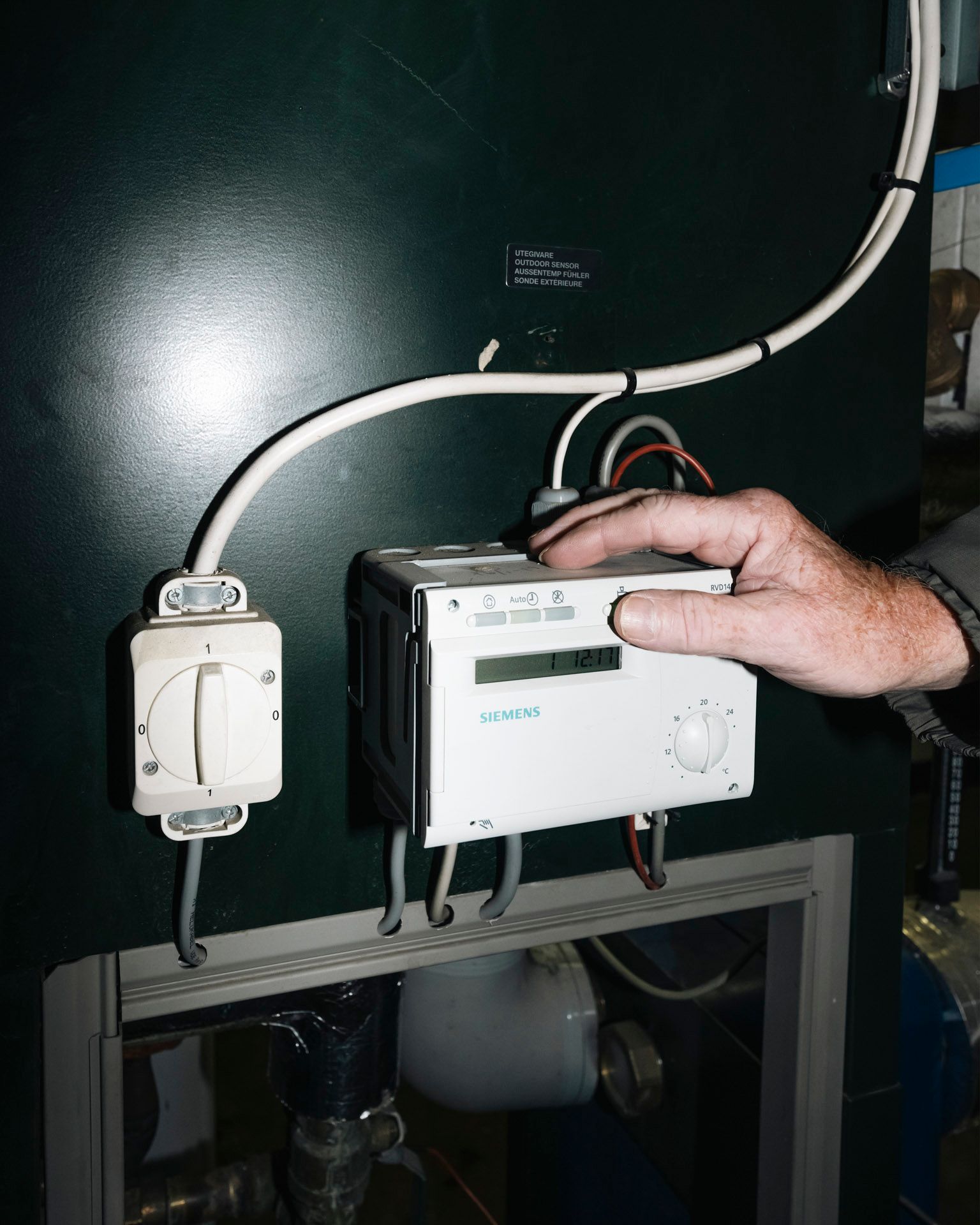 En person justerer en Siemens styringsenhet for oppvarming eller ventilasjon i et teknisk anlegg