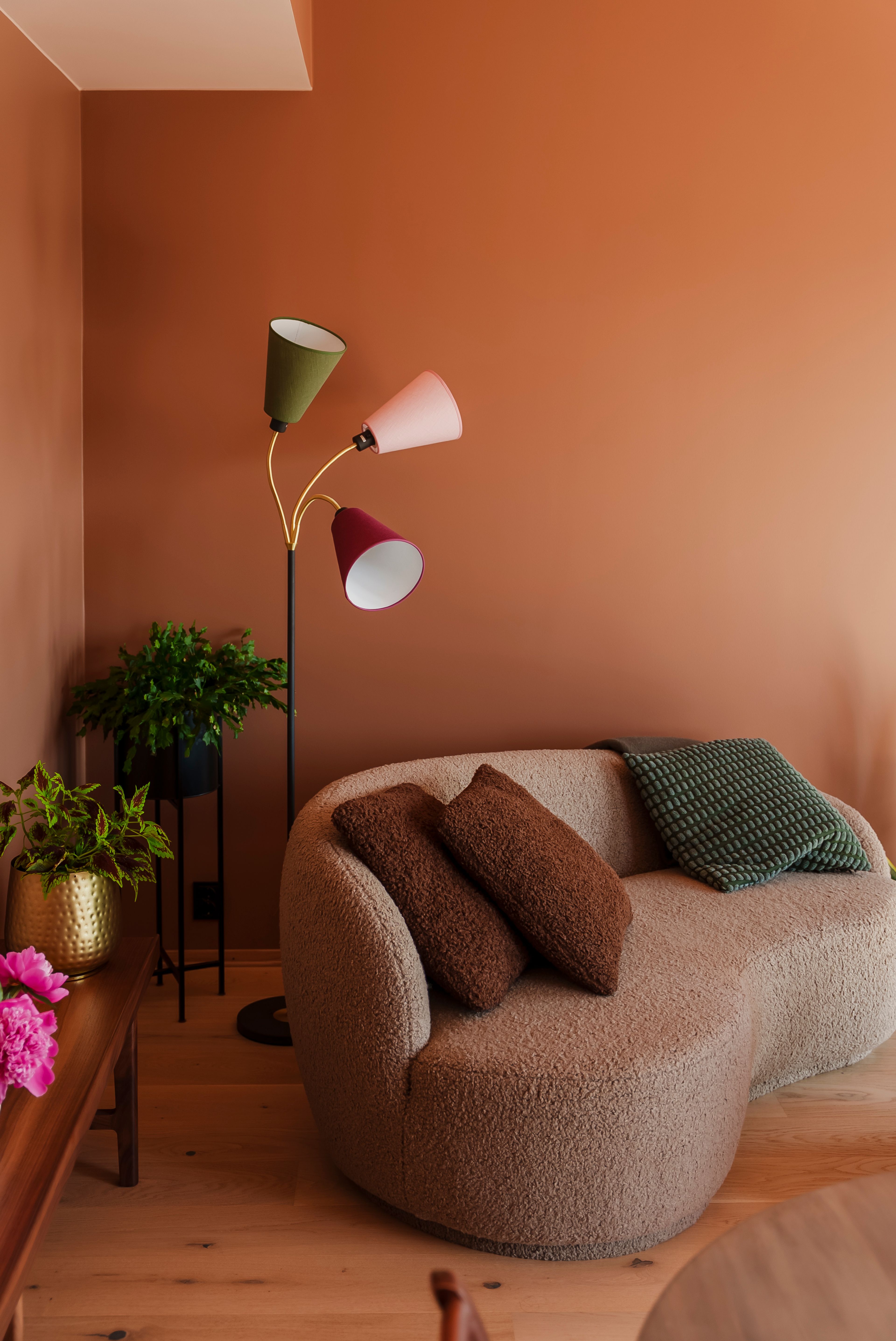 En grå moderne, puffy sofa mot en brun vegg og en fargerik stålampe