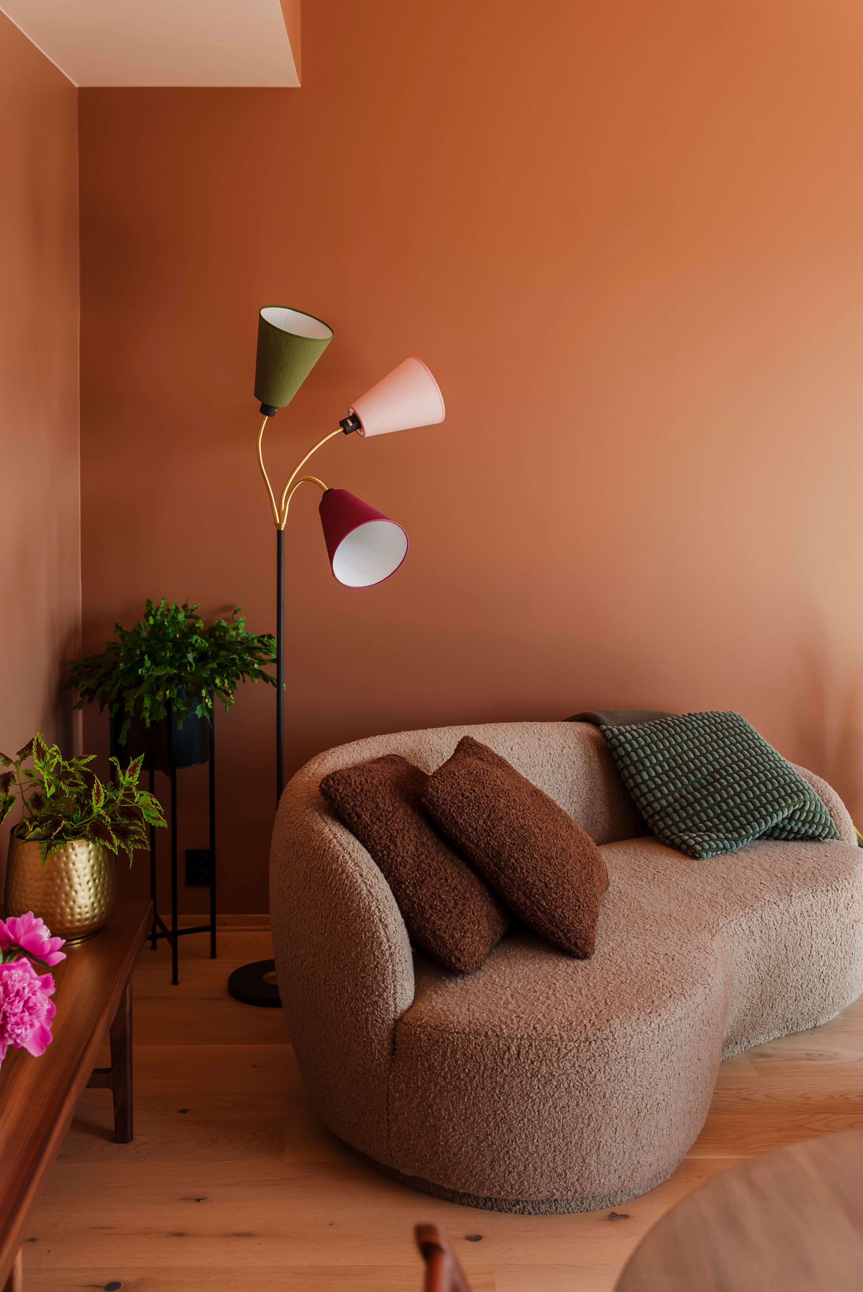 En grå moderne, puffy sofa mot en brun vegg og en fargerik stålampe