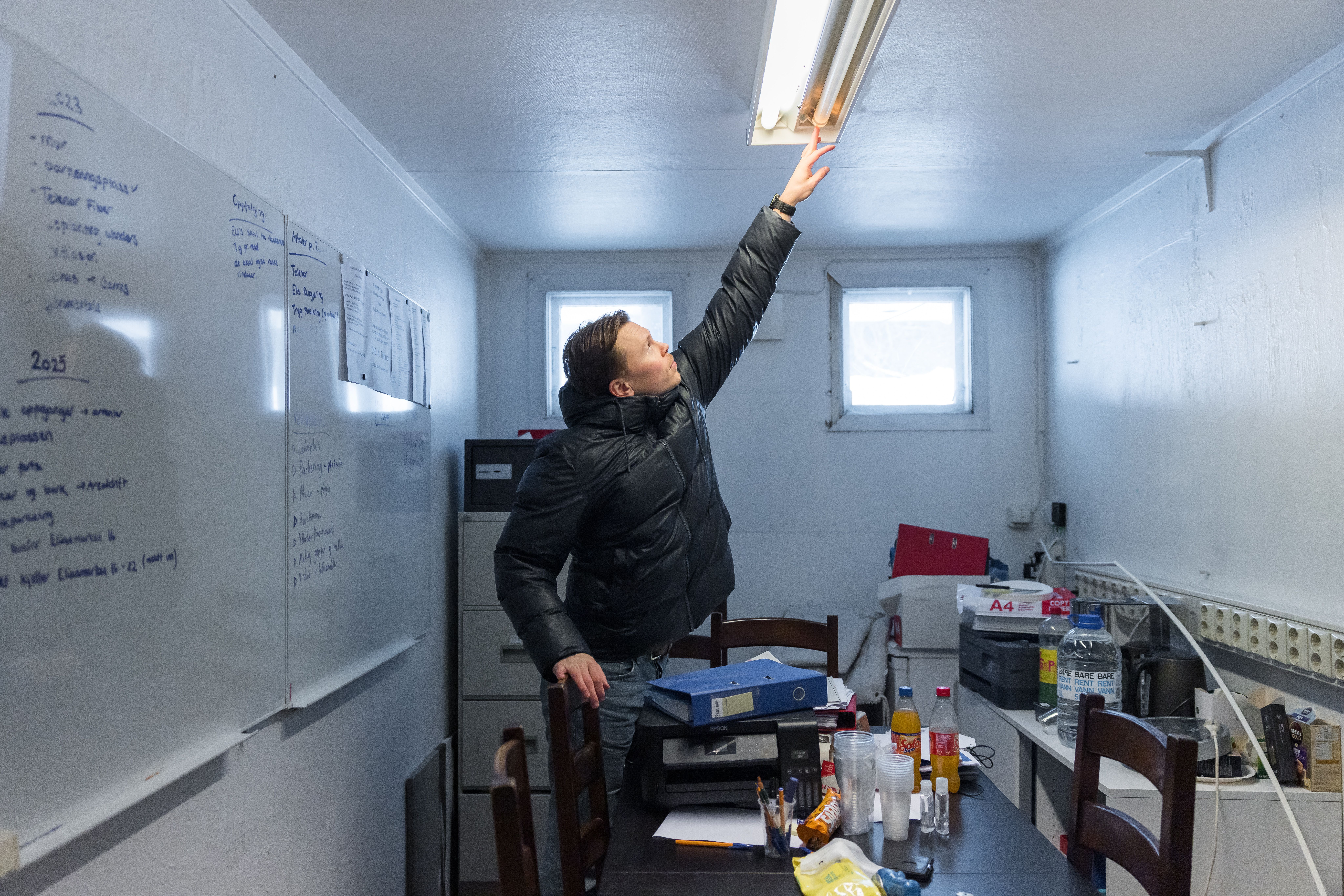 Iben som strekker seg mot taket for å fikse et lysrør.