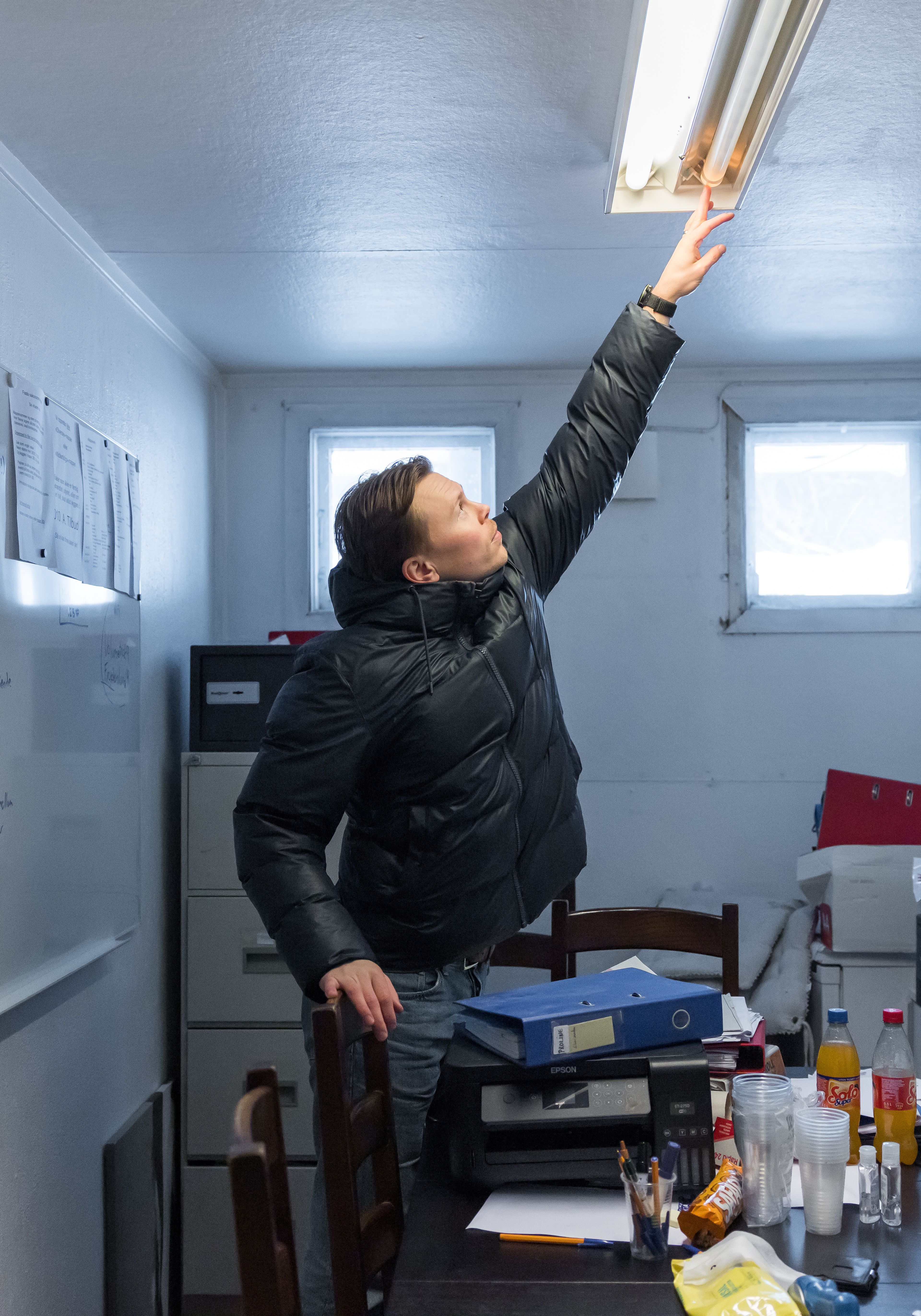 Iben som strekker seg mot taket for å fikse et lysrør.