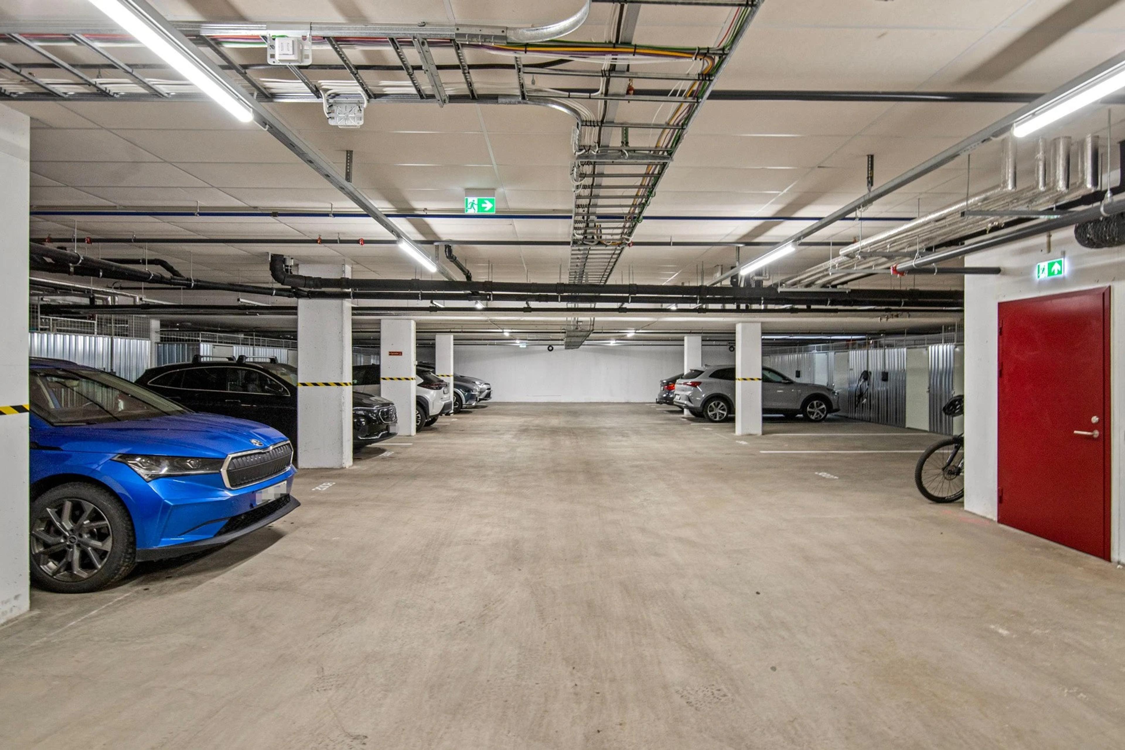 Parkeringskjeller i Teieparken med syv parkerte biler og dør til trapp og heis.