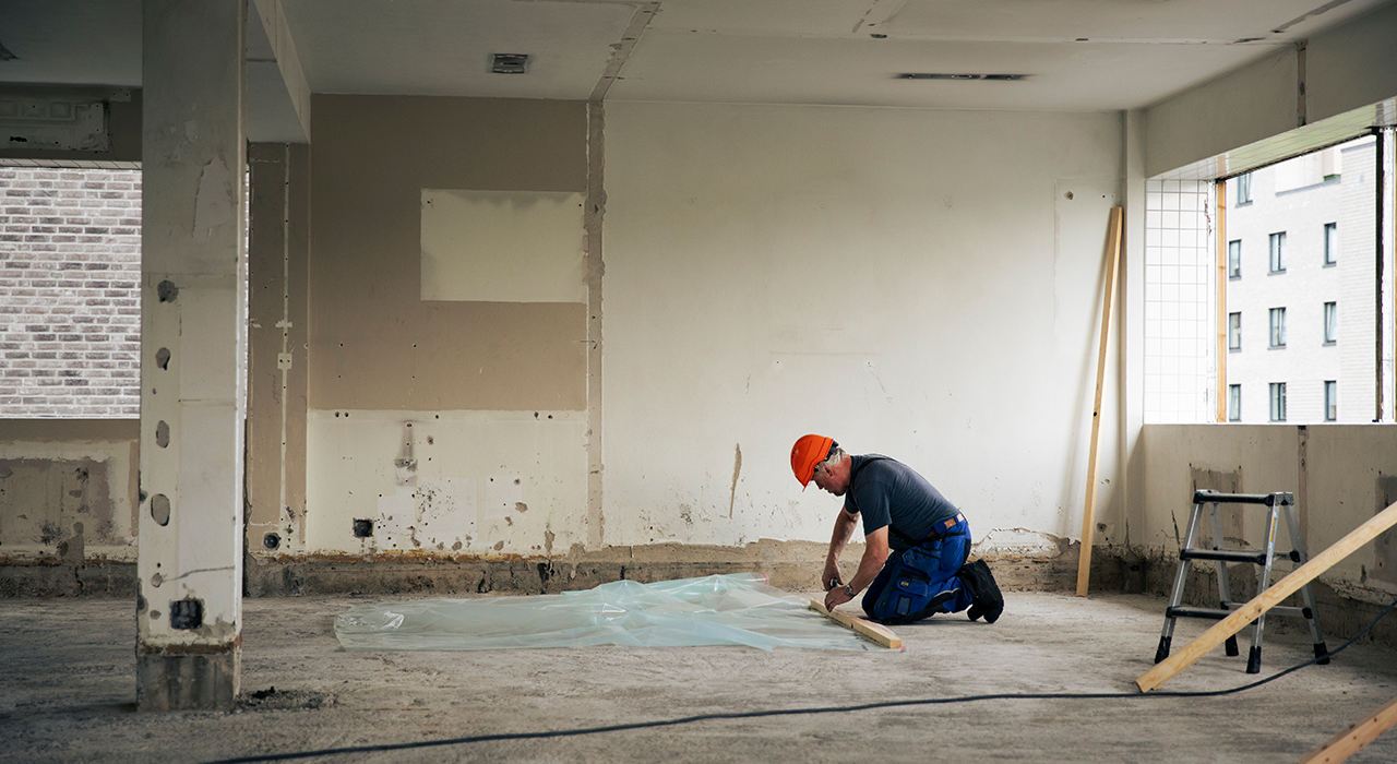 En bygningsarbeider jobber med noe på gulvet i bygget.