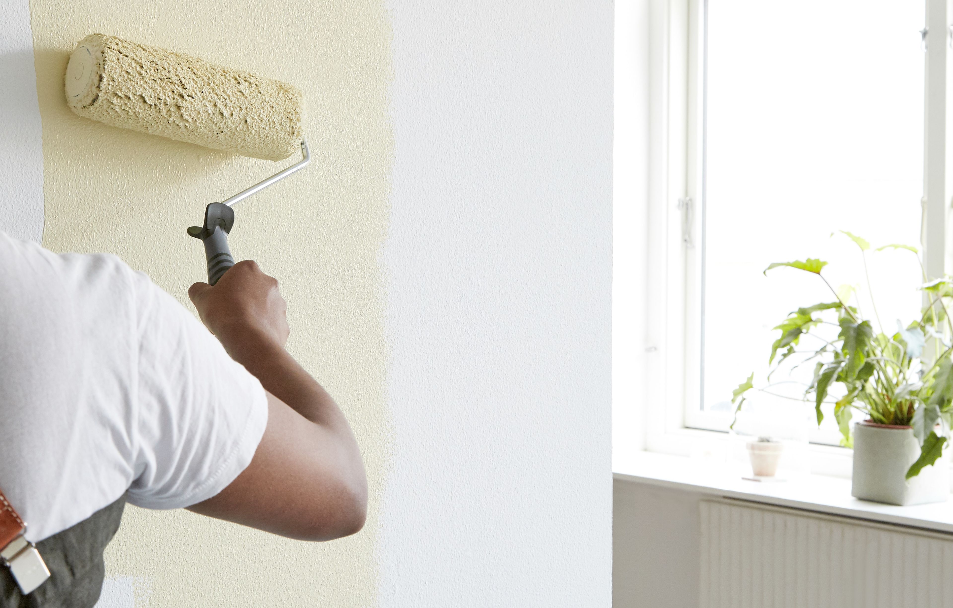 En person maler med malingsrulle og gul maling på en hvit vegg