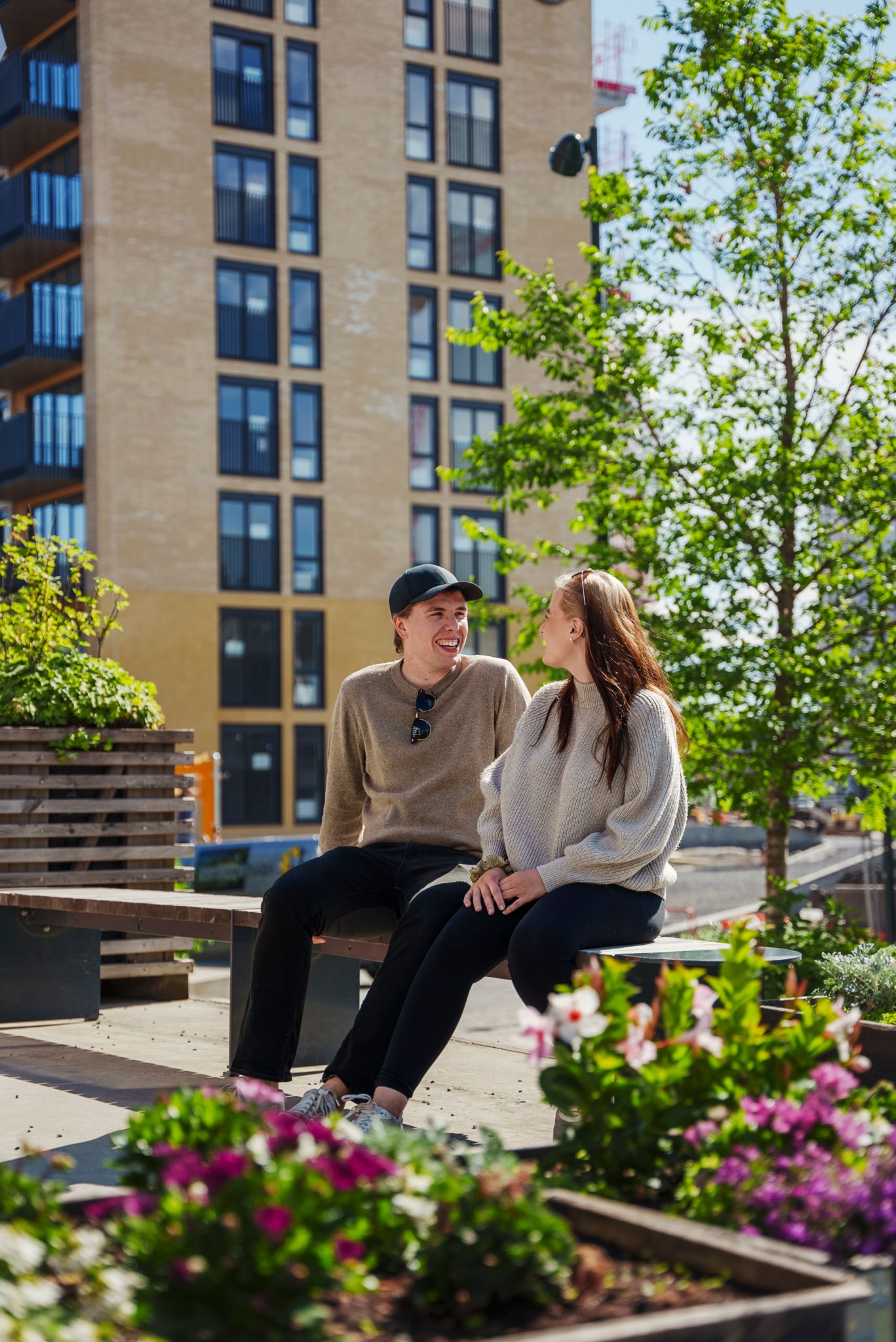Lars Erik Jensen og Martine Nydahl Svehagen på en benk mellom blokker på Ulven, omgitt av blomsterbed og trær.