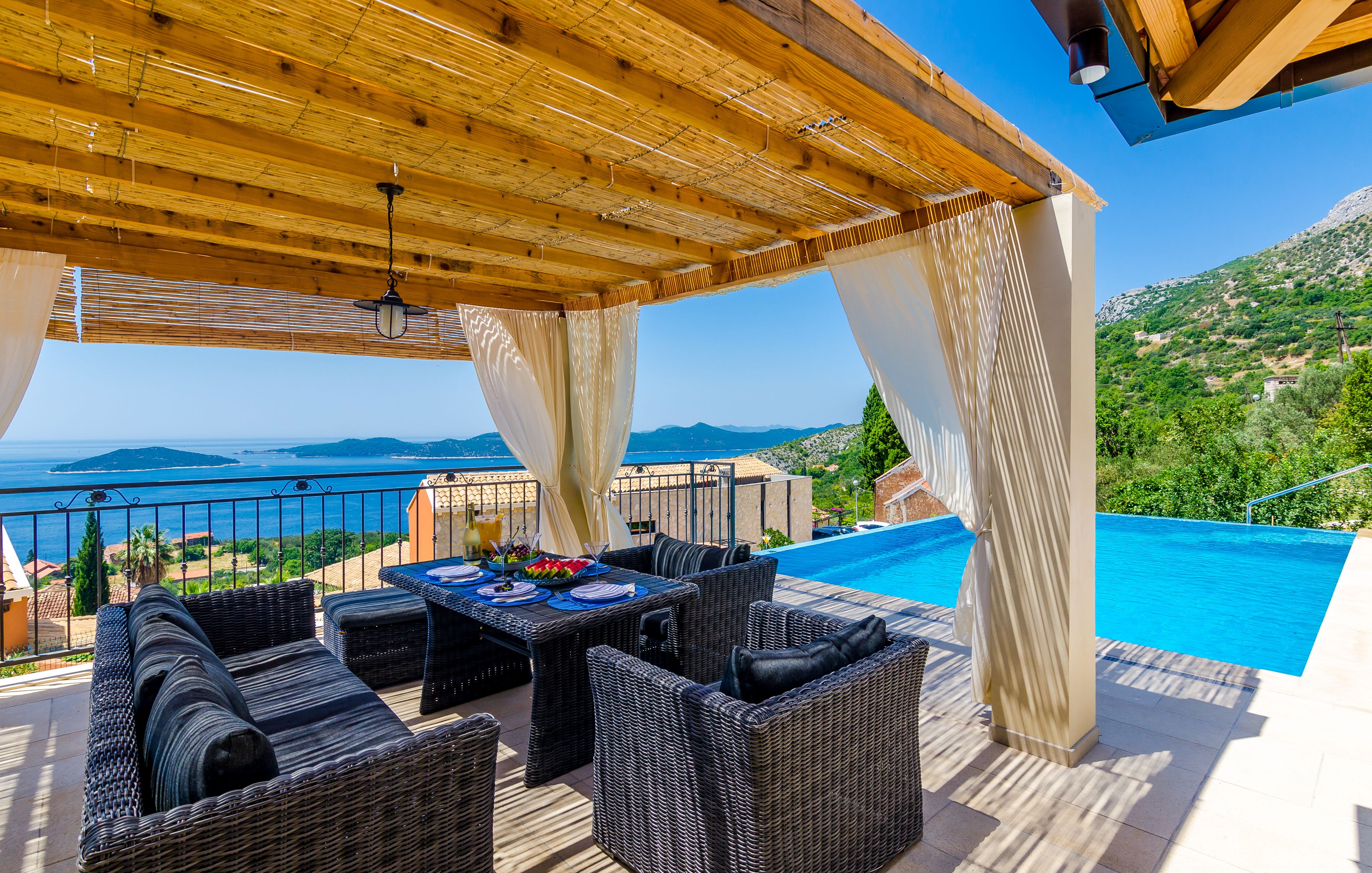Terrasse med sofalounge, pergola, badebasseng og utsikt mot havet.
