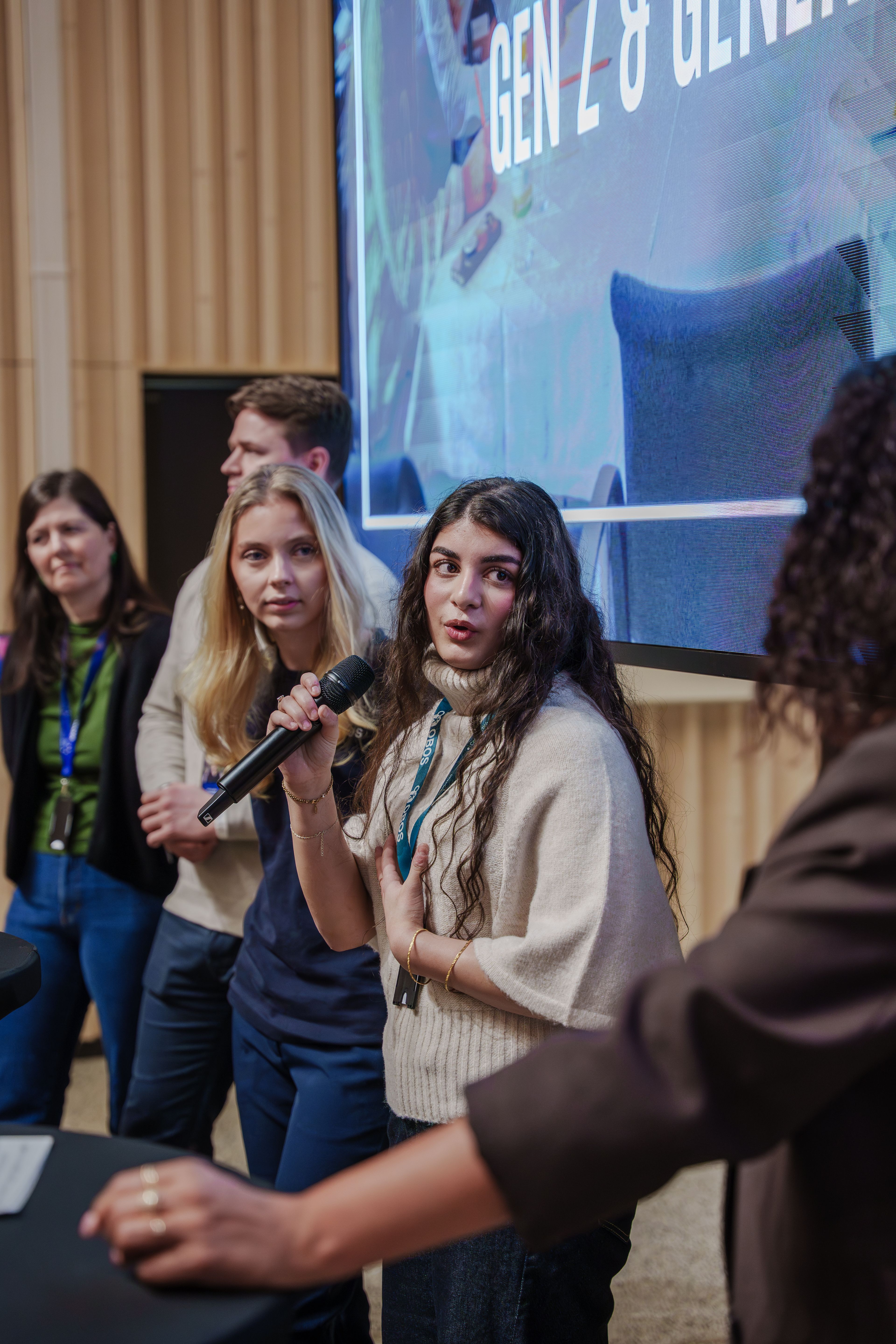 To unge jenter taler til en forsamling, hvor hun ene holder en mikrofon