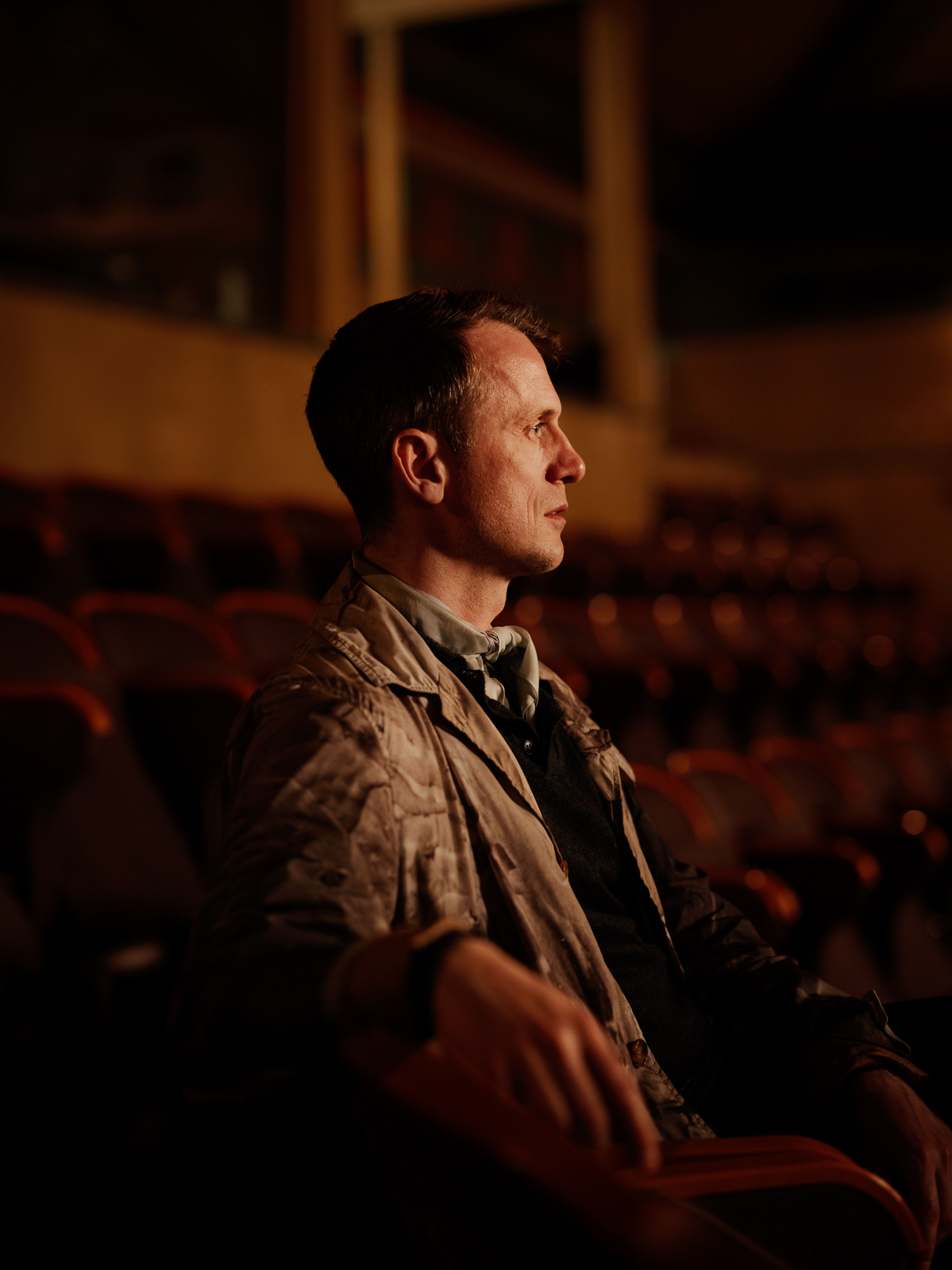 Nils Bech i profil i den dunkelt belyste salen til Centralteatret. Høyre side av ansiktet peker mot kamera, og han stirrer rett frem.