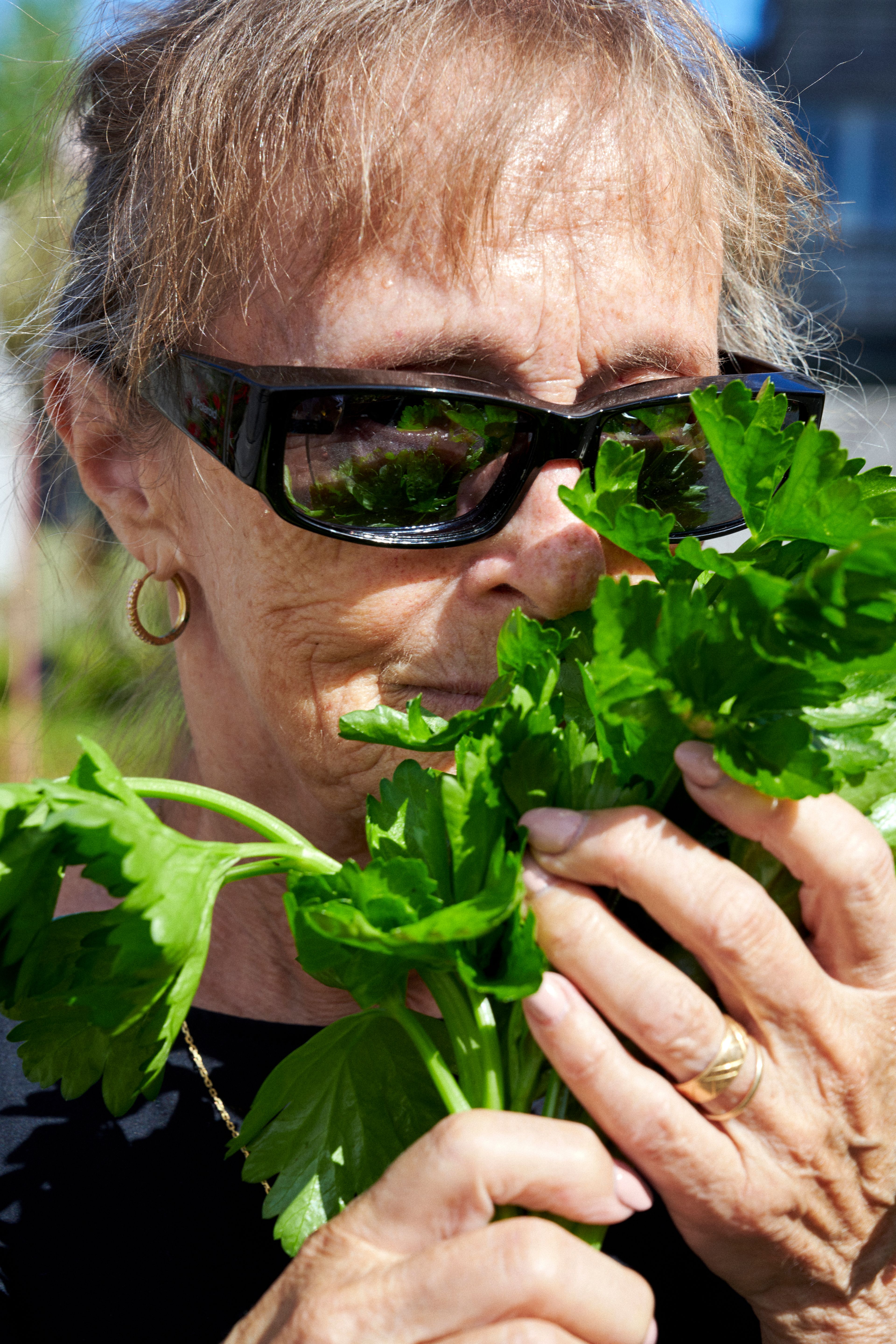 Kvinne med solbriller holder noen urter i hånda som hun lukter på.