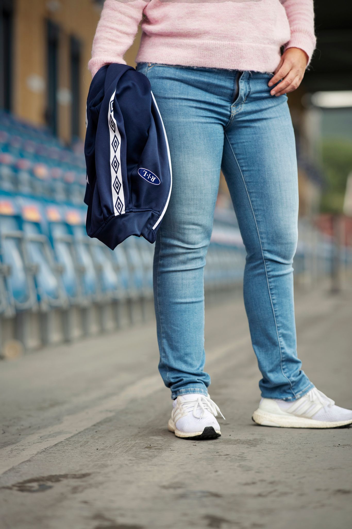 Nærbilde av Stinas bein foran tribunen, hvor hun har den ene hånden i lommen og holder en treningsjakke i den andre.