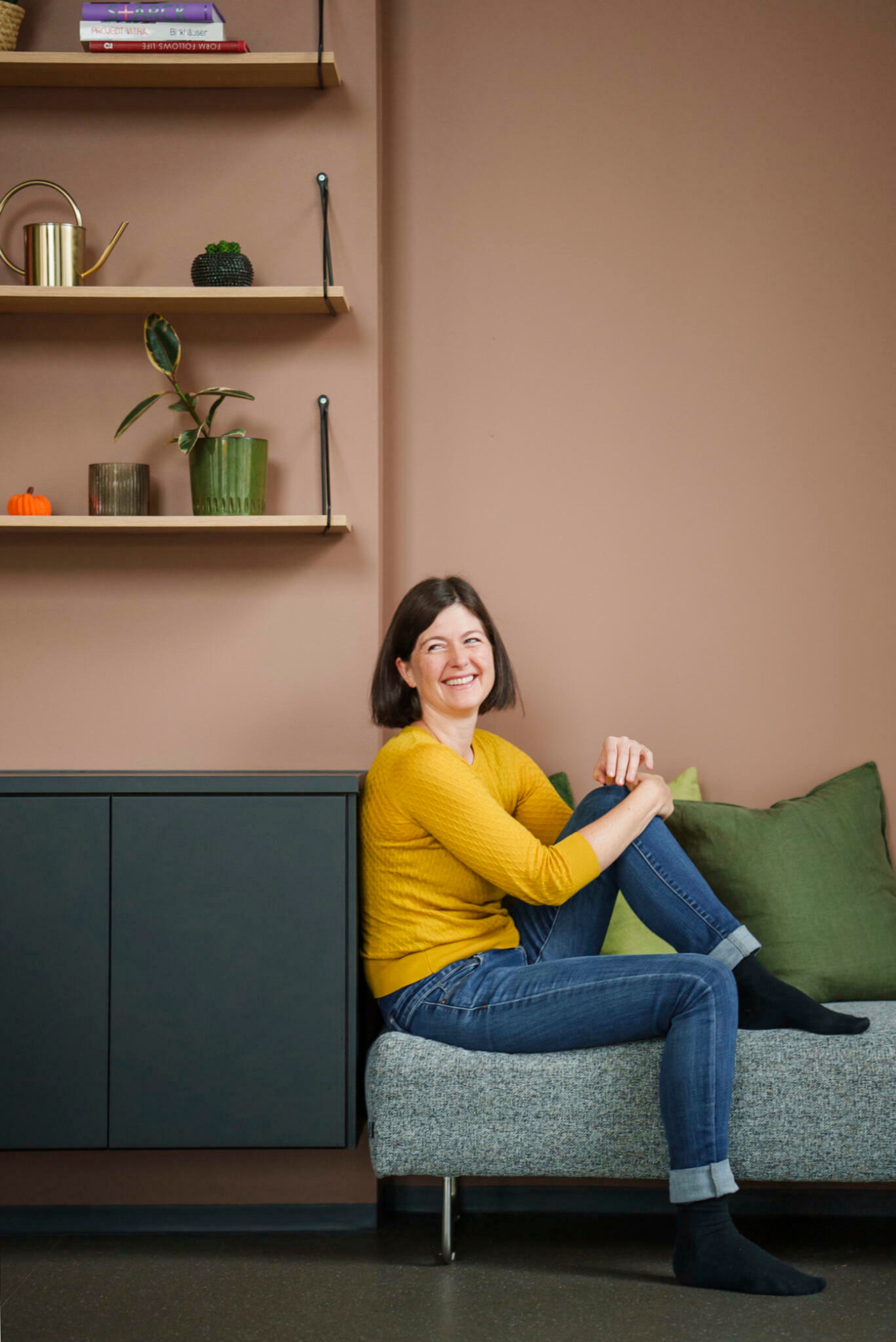 Ulvens nabolagsvert Katrin Schauer sitter i en grå sofa i et ferskenmalt rom