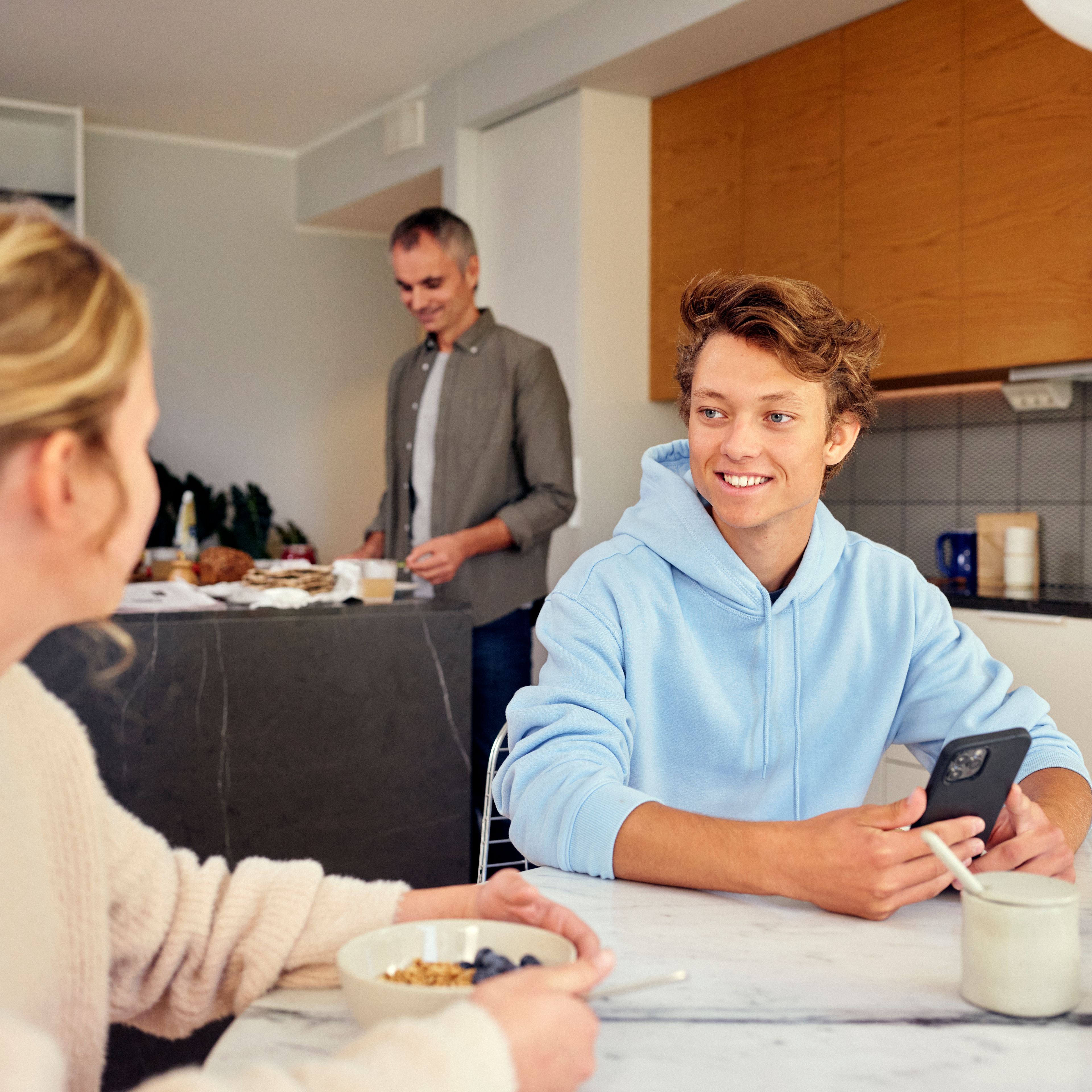 smilende gutt som sitter med telefonen i hånden og snakker med foreldrene sine