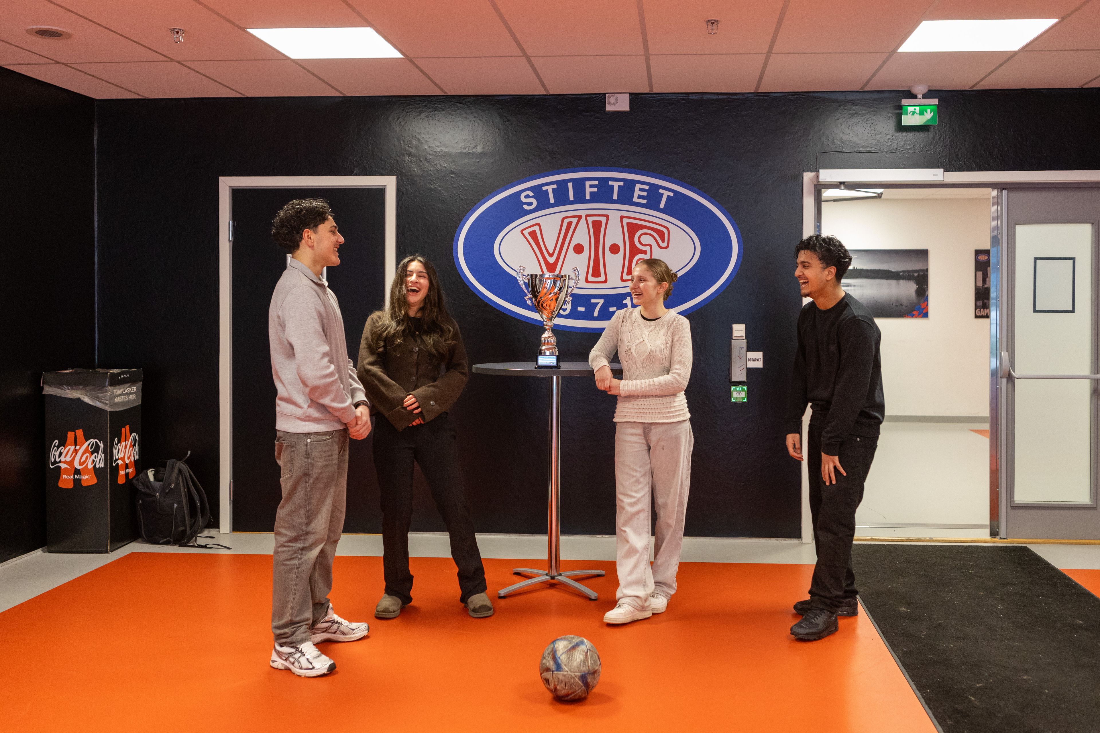 Fire ungdommer står inne på Intility Arena, med Community Champions League-pokalen mellom seg.