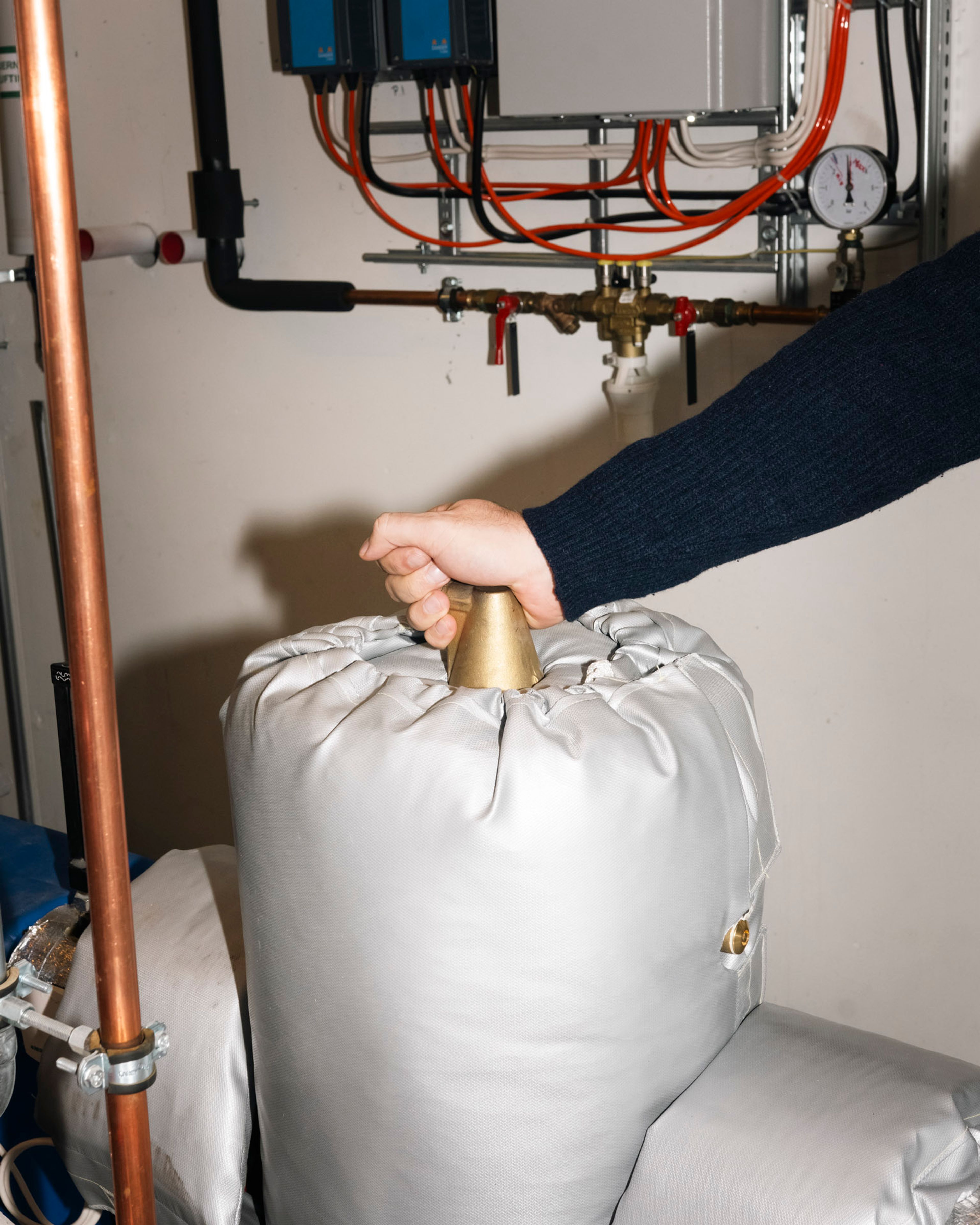 Hånd løfter isolasjonspute på rør i teknisk rom for å redusere varmetap