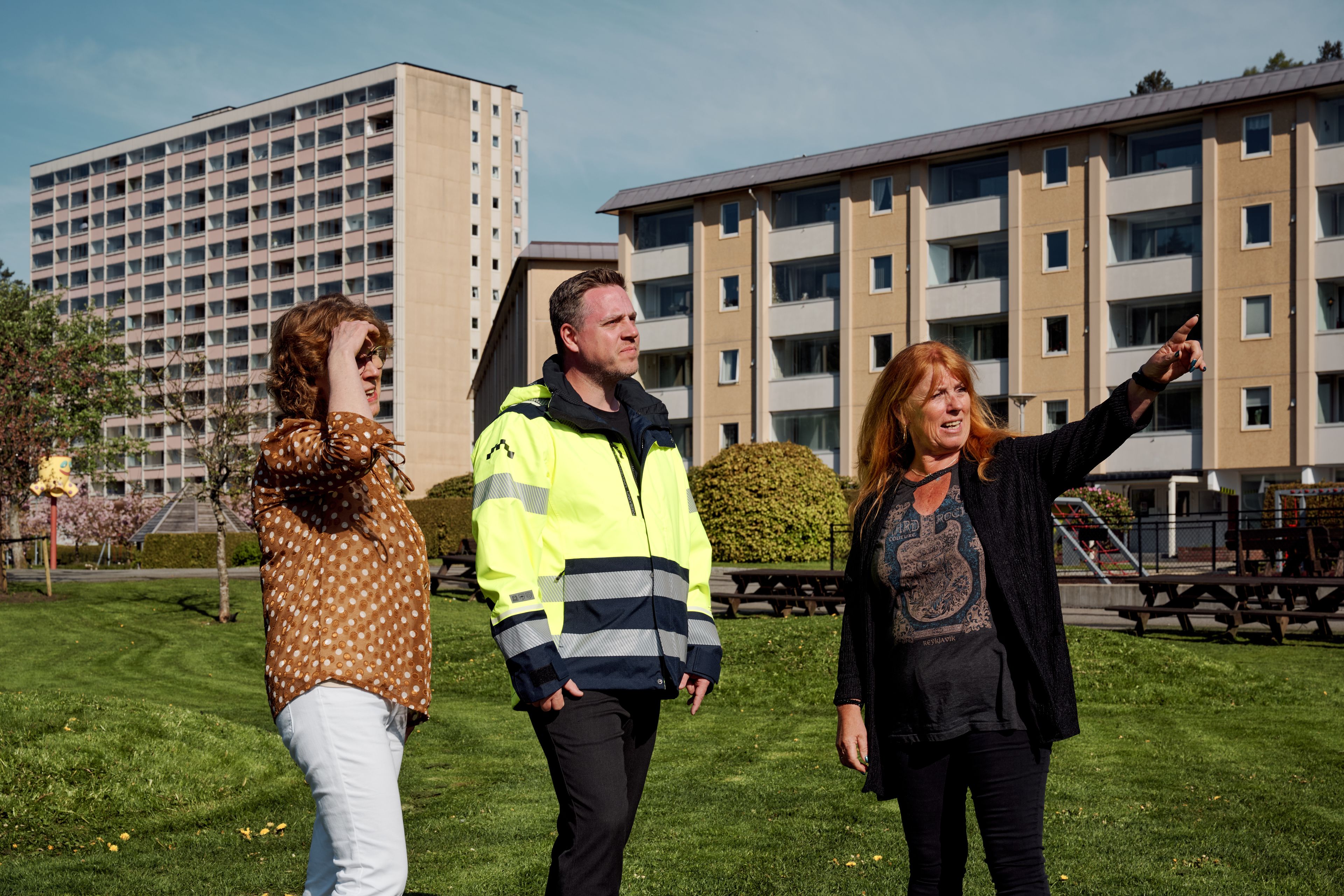 Tre personer står utenfor en boligblokk. En av de peker mens de andre følger med.