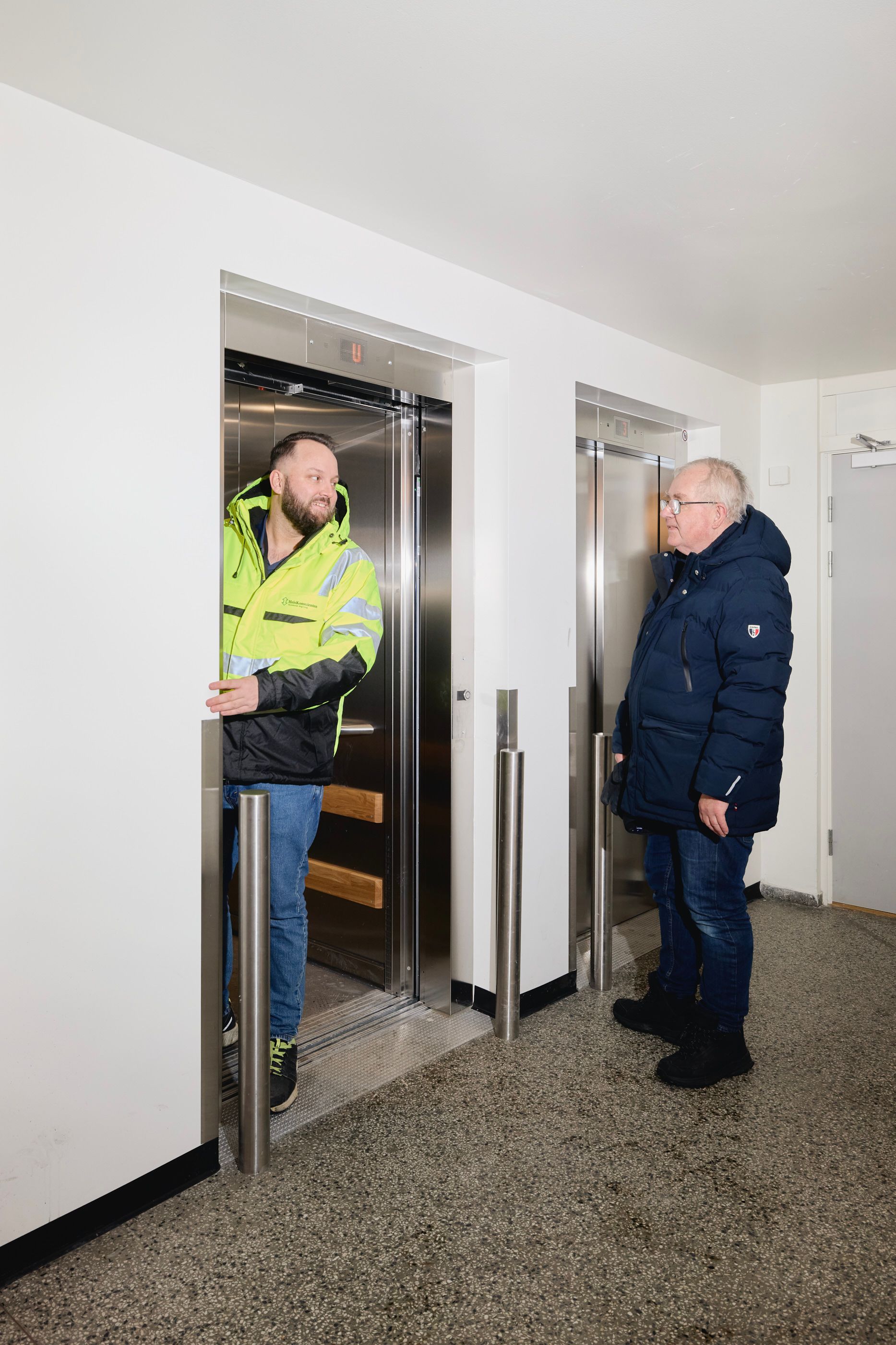 To menn utenfor en nymontert heis i et borettslag