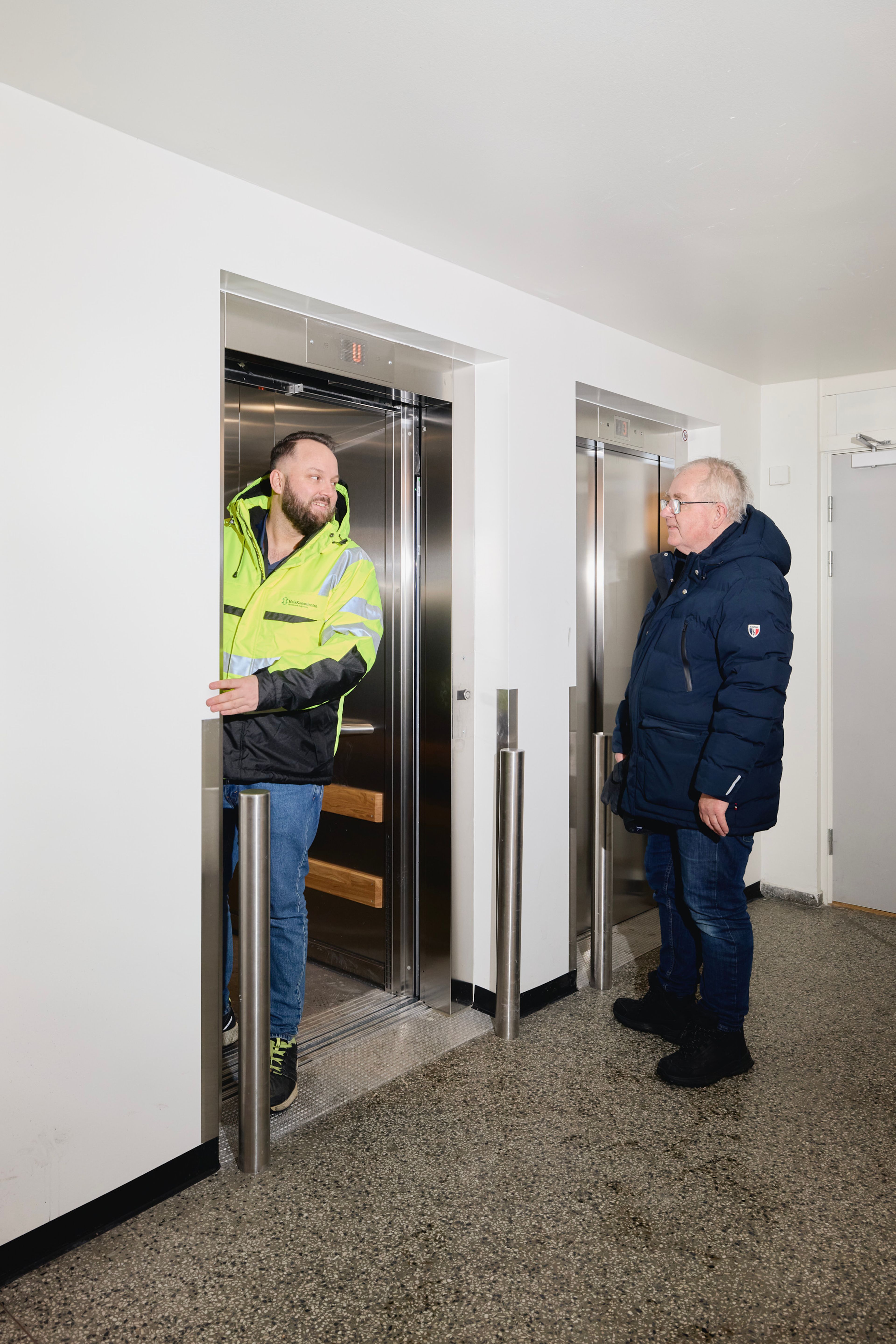 To menn utenfor en nymontert heis i et borettslag