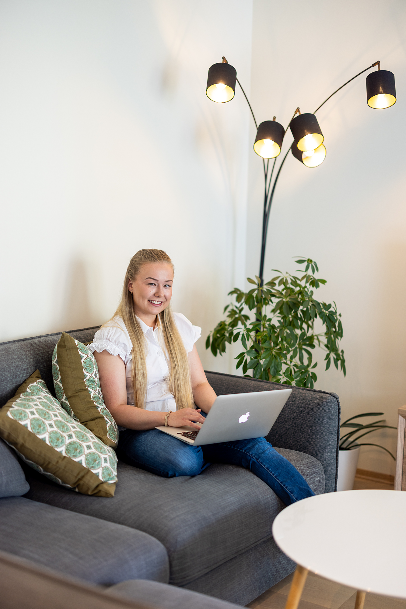 Amanda sitter i en grå sofa i stuen, med PC i fanget og smiler inn i kamera.