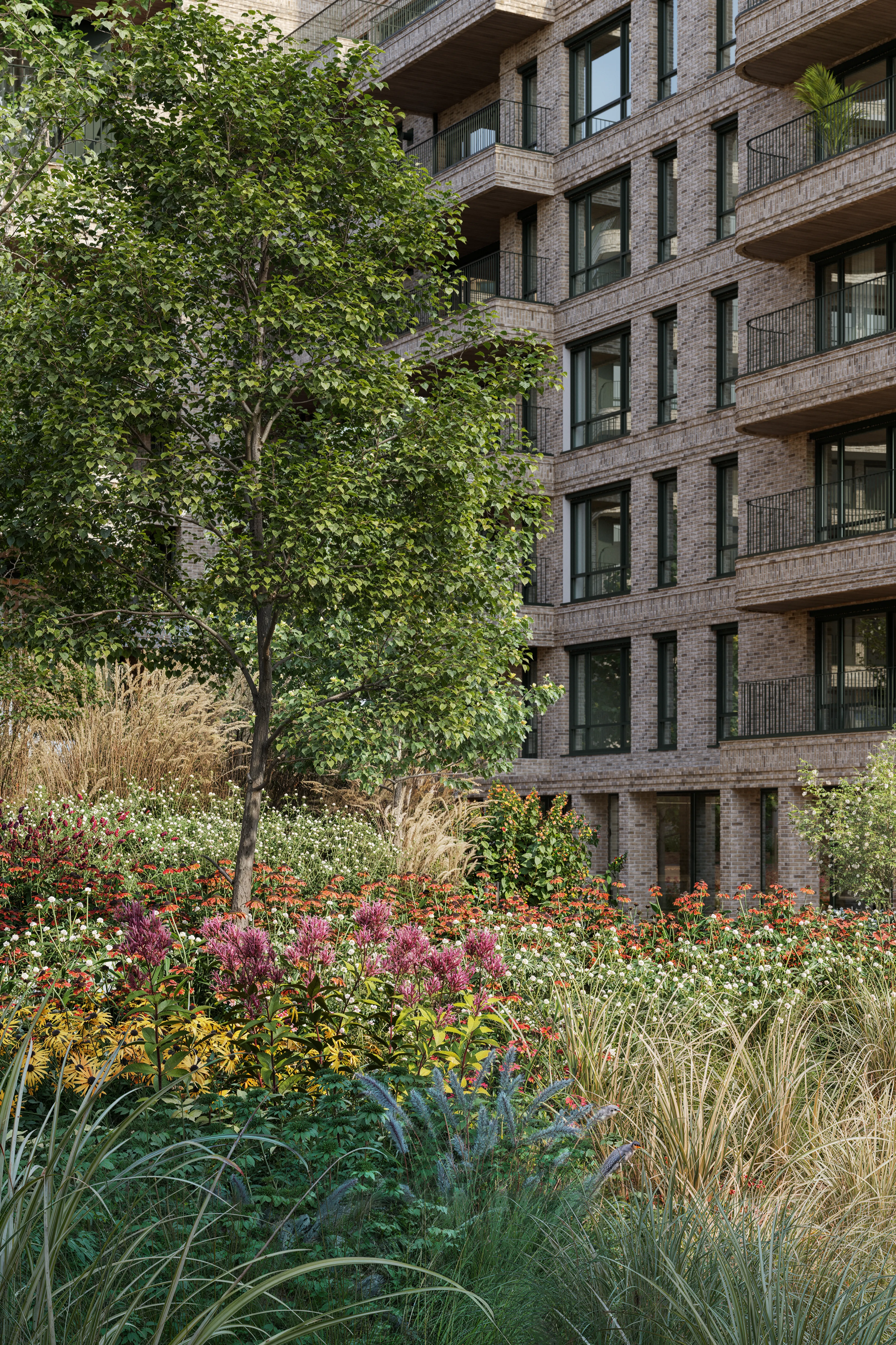 Et stort tre og mange blomster utenfor boligbygg