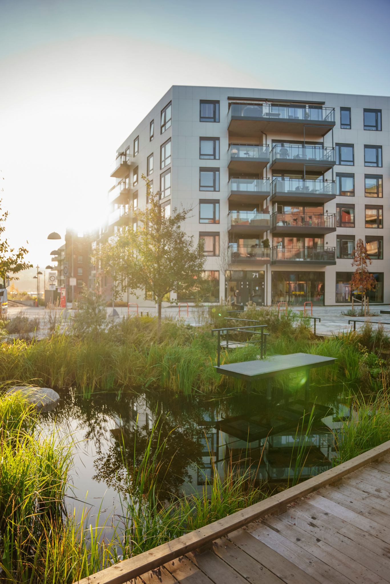 Bilde av fasaden til et leilighetsbygg med et vannspeil og gangvei i tre foran
