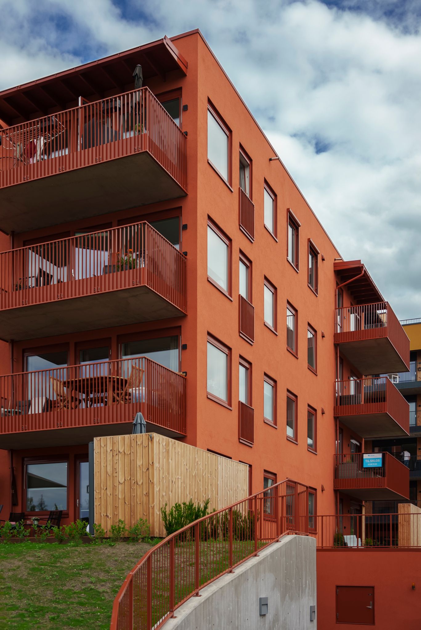 Bilde av et rødt leilighetsbygg med balkonger og grønn plen utenfor