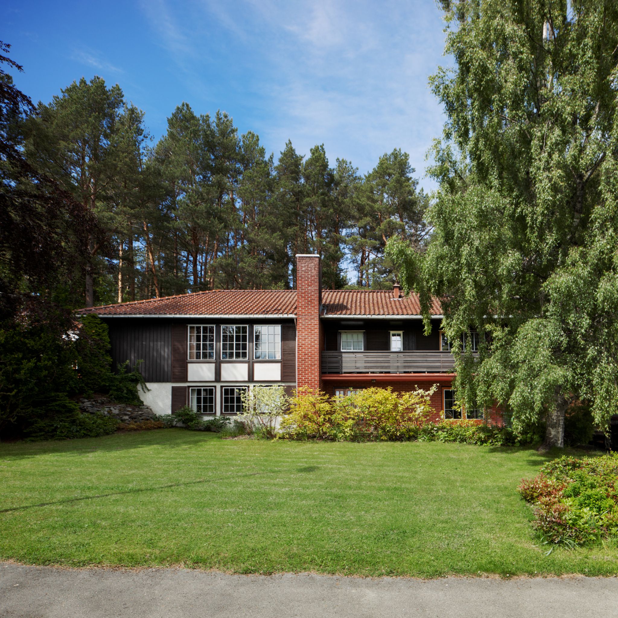 Et block watne-hus pipa plassert midt i huset, og med plen og trær rundt huset.