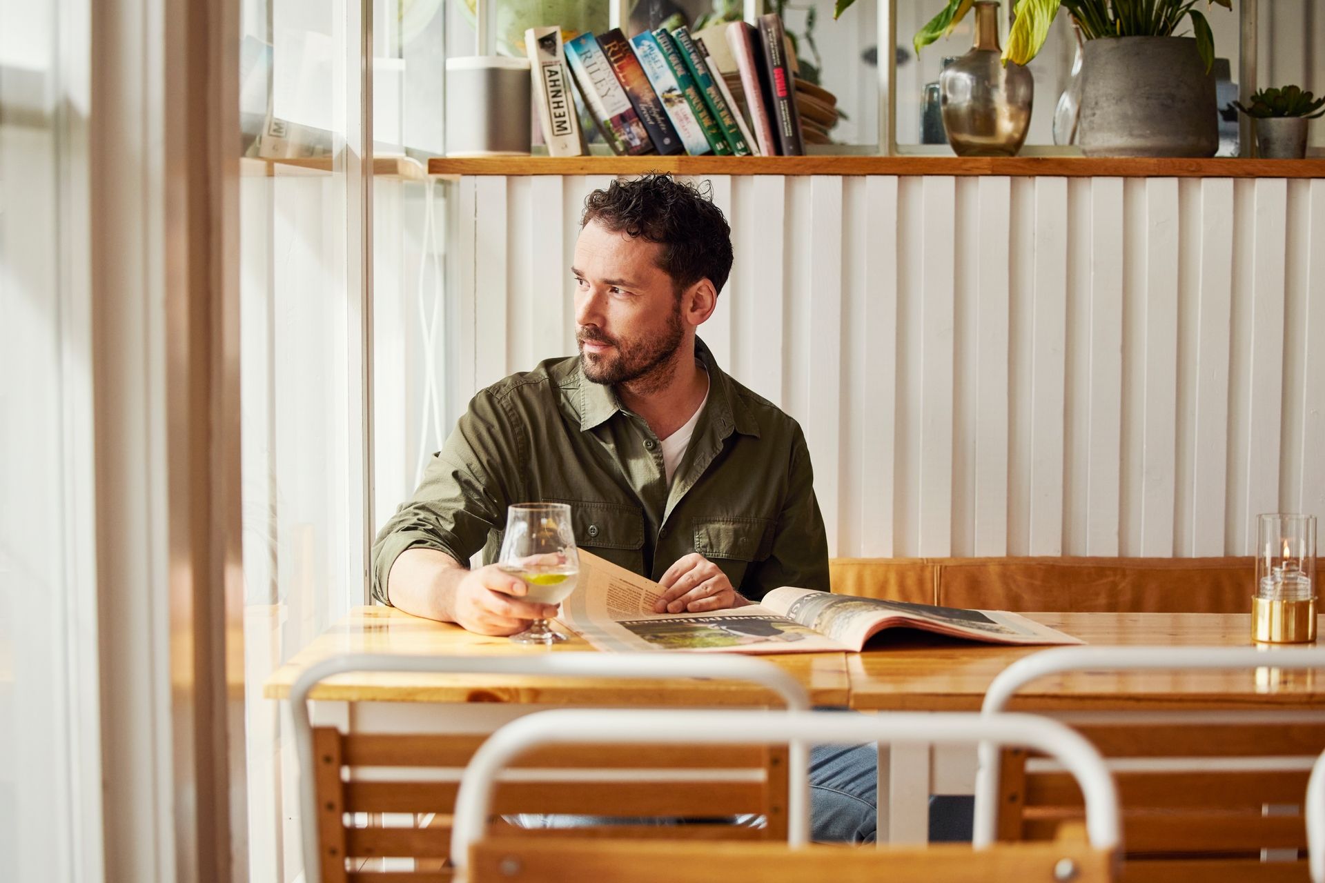 Mann som sitter på en café med et glass i hånda ved Sjøflyhavna på Fornebu