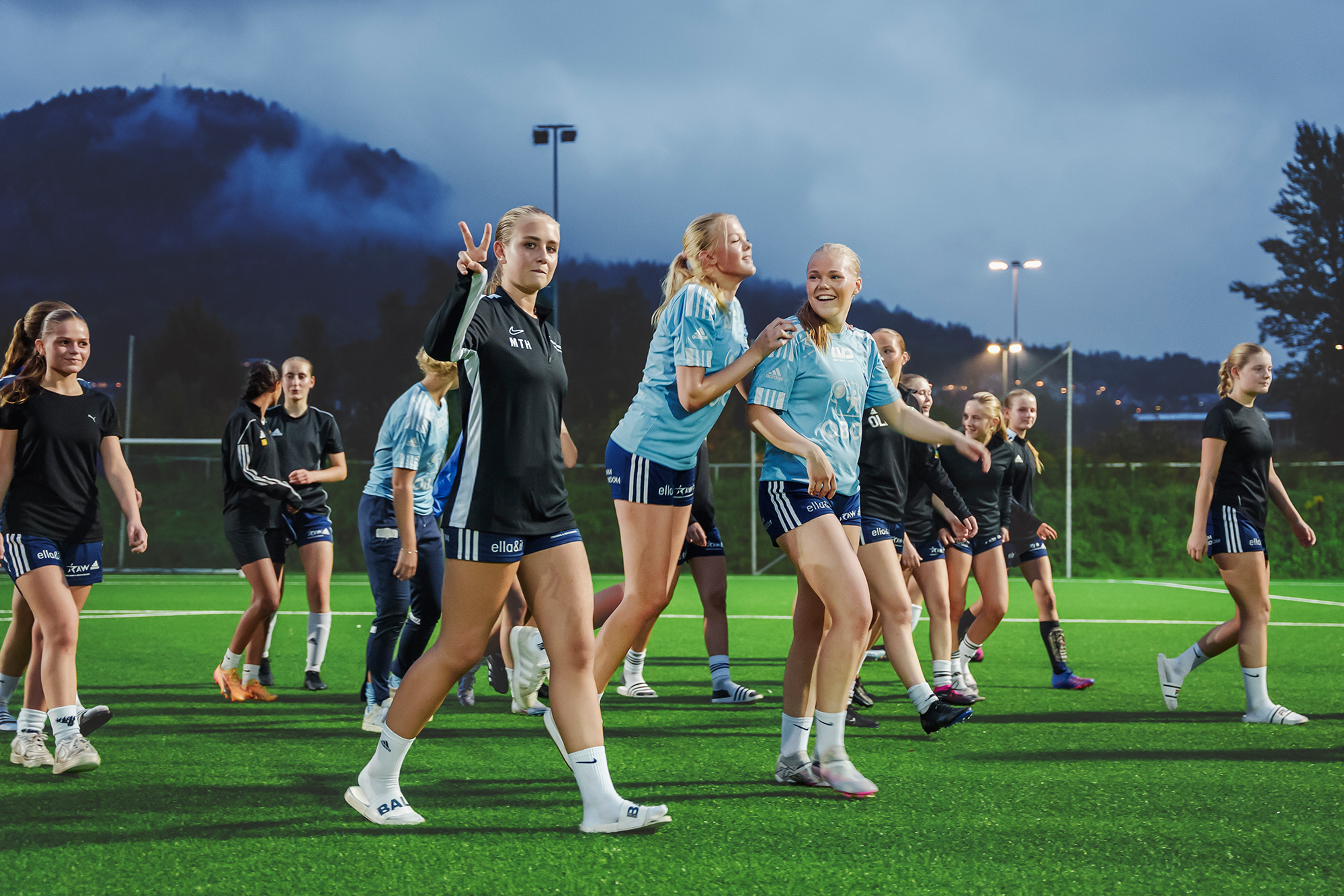 Jentene i UBK går i gruppe og ler og morer seg med hverandre på en kunstgressbane.